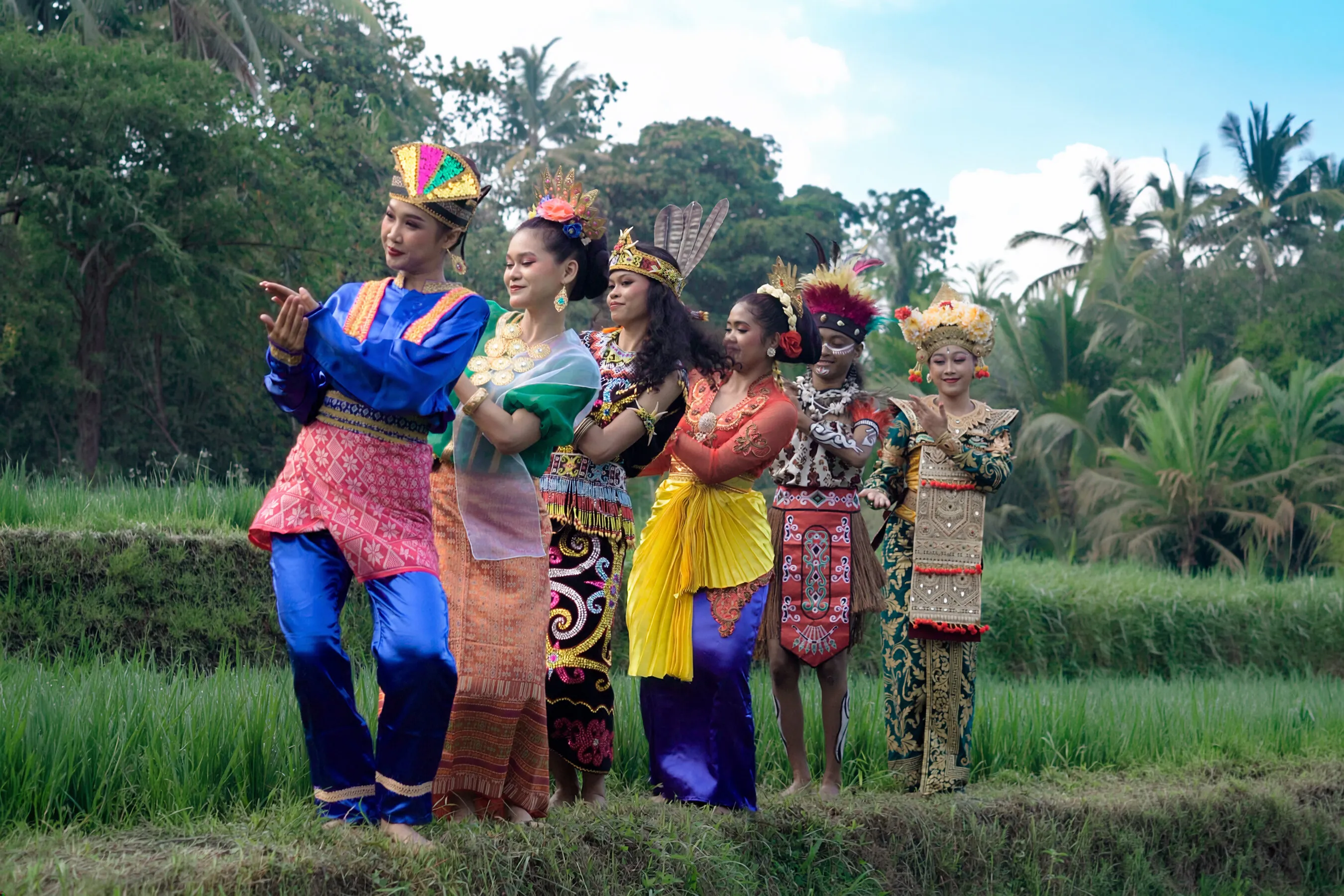 Six performers in colorful traditional dress dance in a lush rice field.