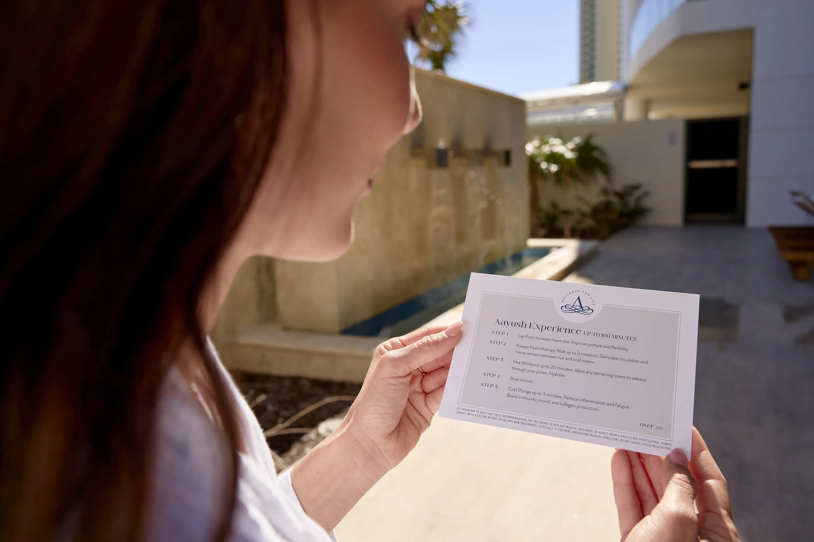 A person holds an Amrit Ocean Resort Spa treatment instruction card by a pool.