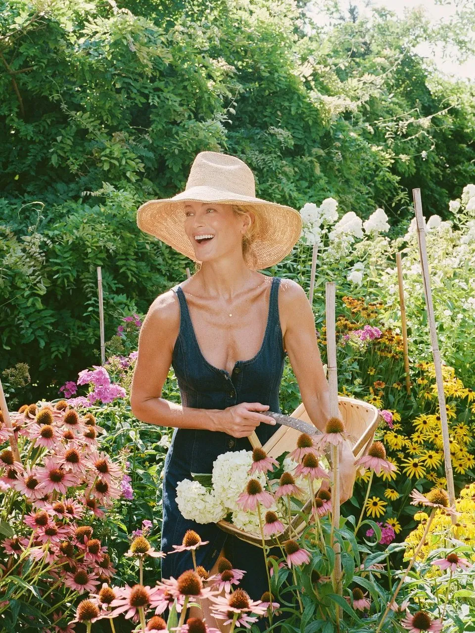 Carolyn Murphy in a sunhat holding a basket of flowers in a garden.