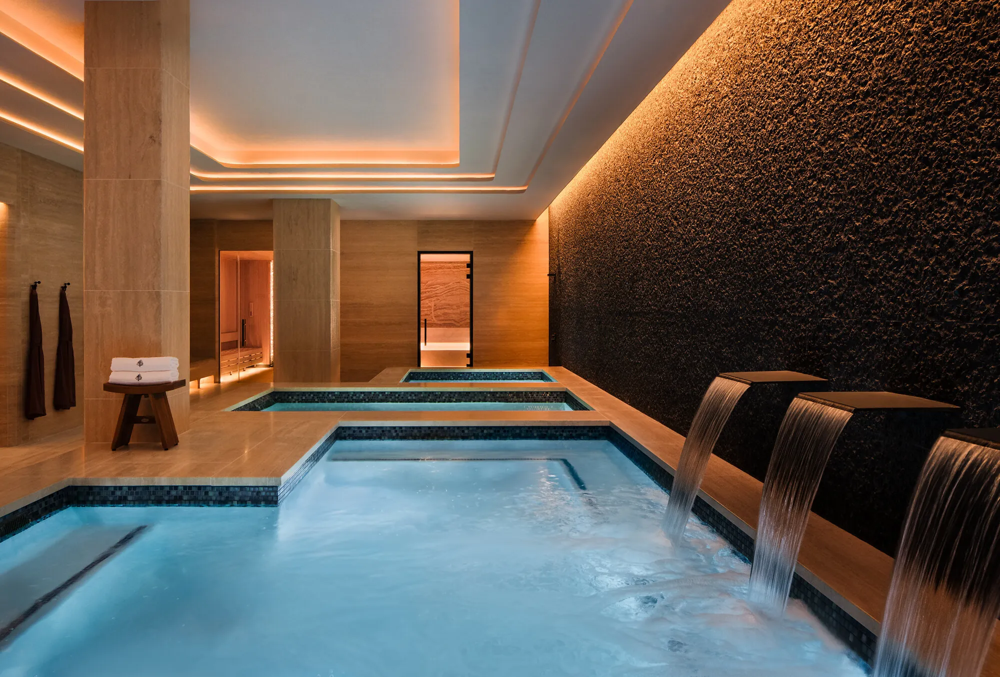 Indoor spa pools with waterfall features, tiled walls and warm recessed lighting