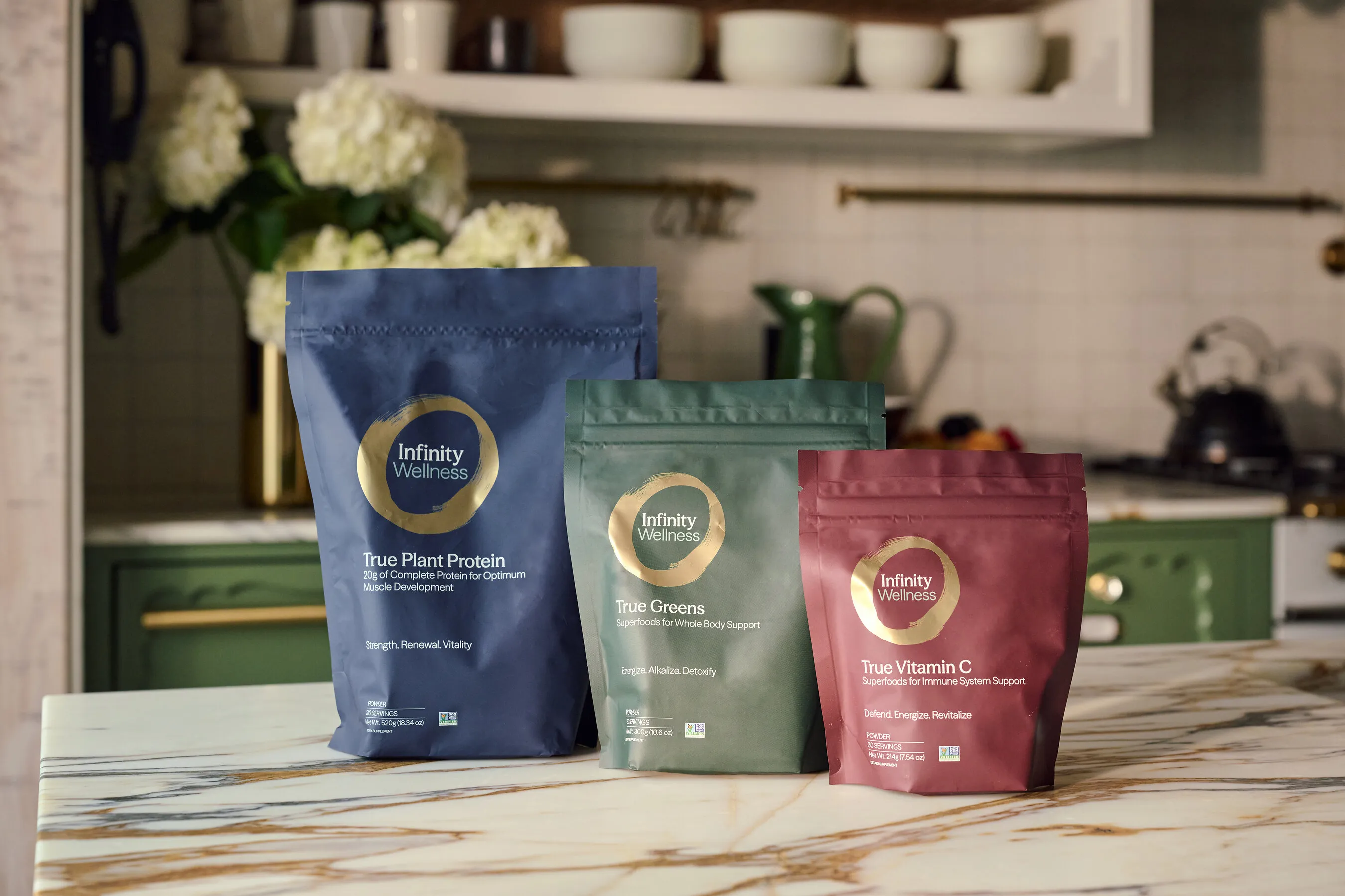 Infinity Wellness True Plant Protein, True Greens and True Vitamin C pouches on a kitchen counter.