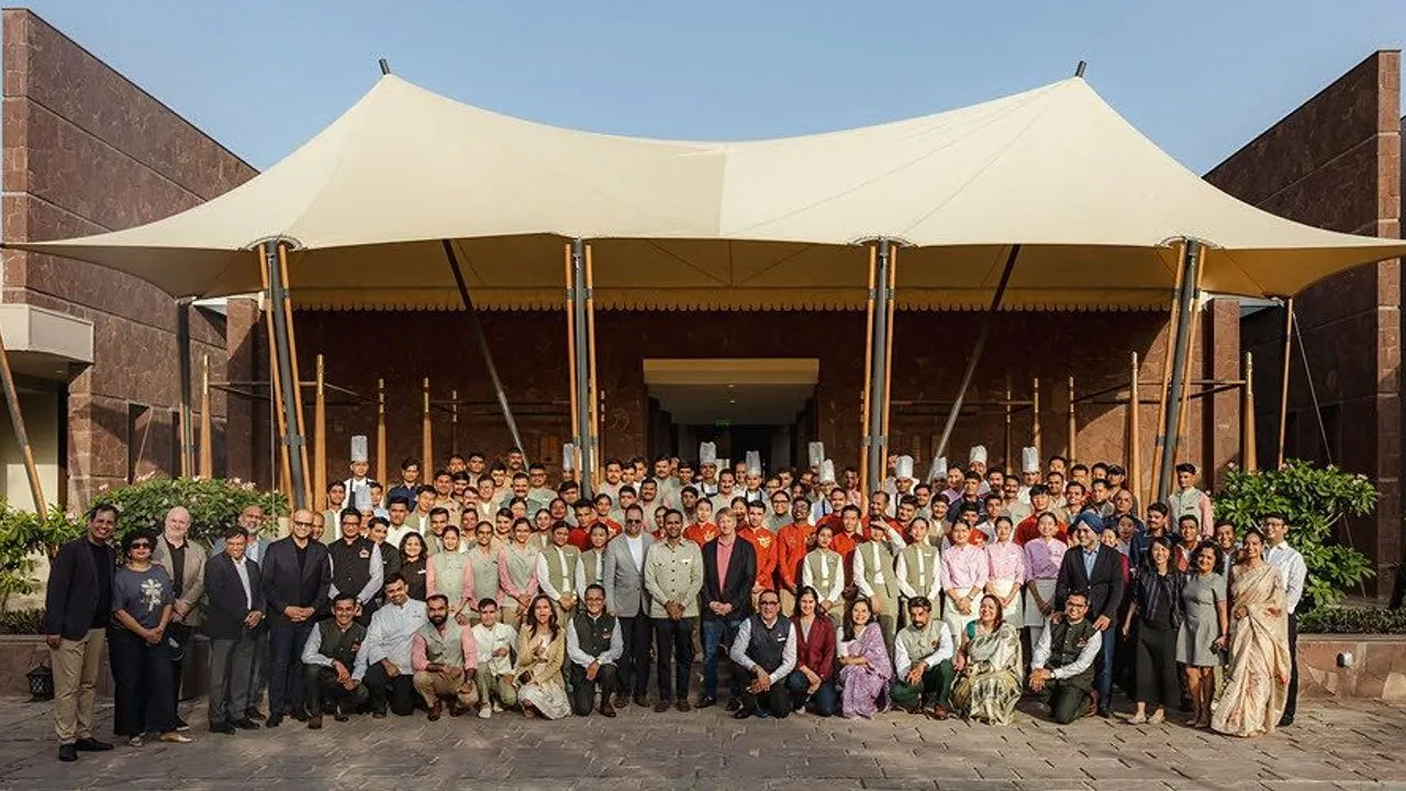 A large group gathers outside a hotel entrance beneath a cream canopy.