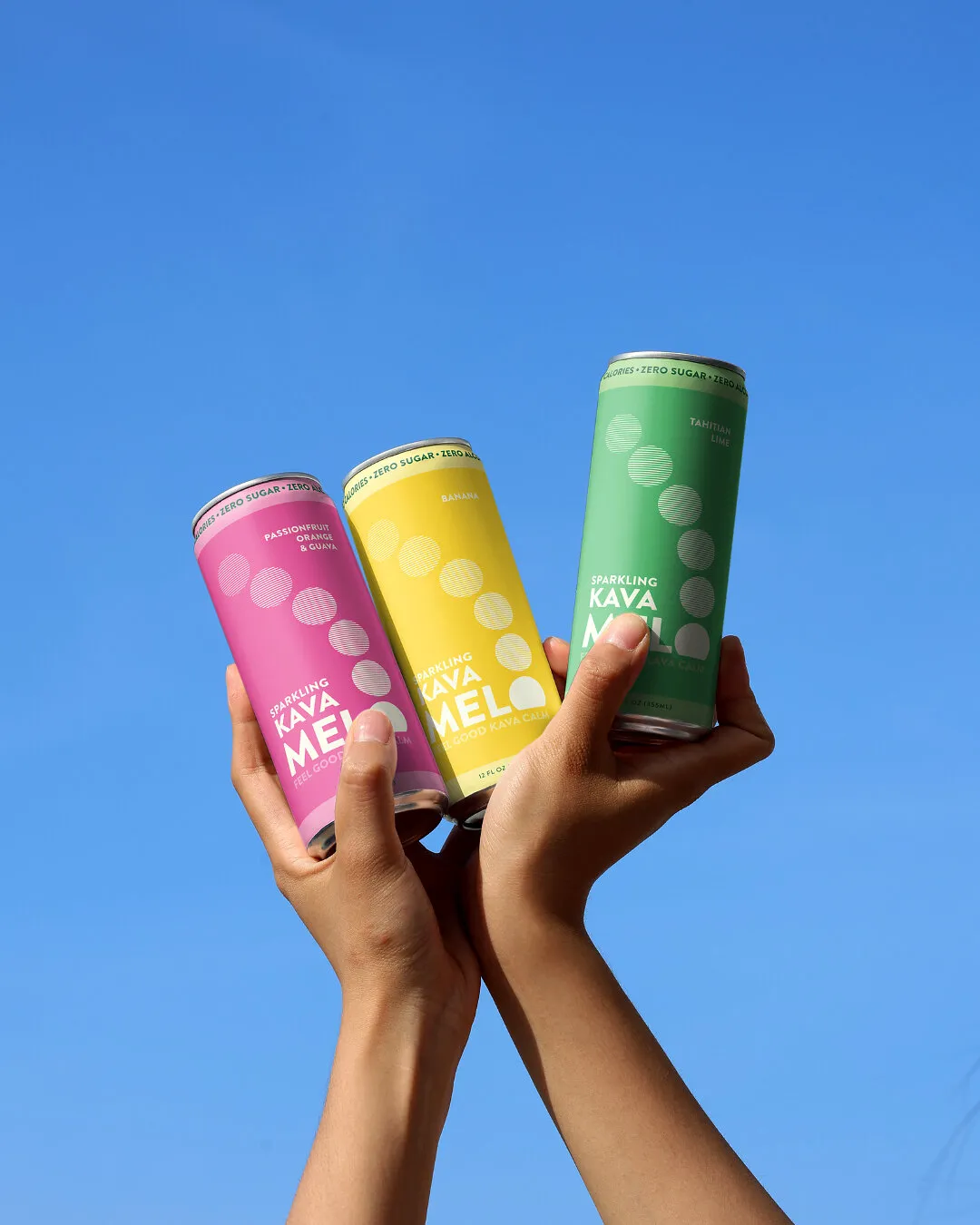 Three hands hold pink, yellow and green cans of Melo Kava sparkling drinks against a blue sky.