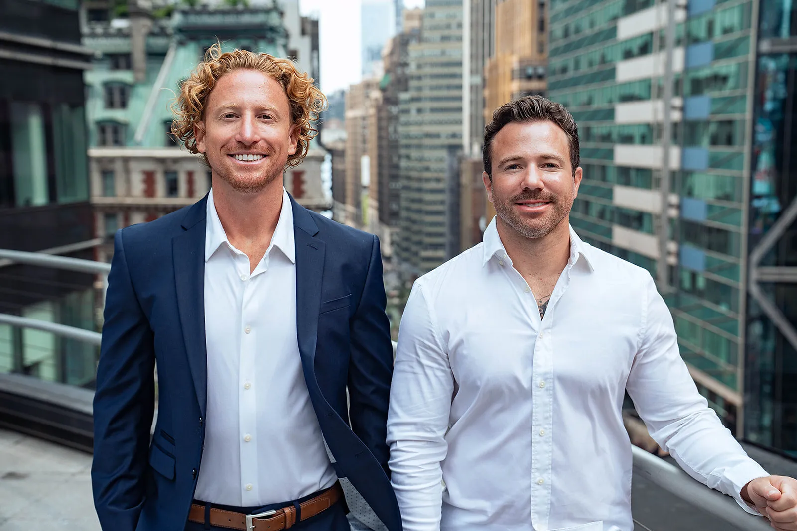 Two people standing among city office buildings, one in a navy suit and one in a white shirt.