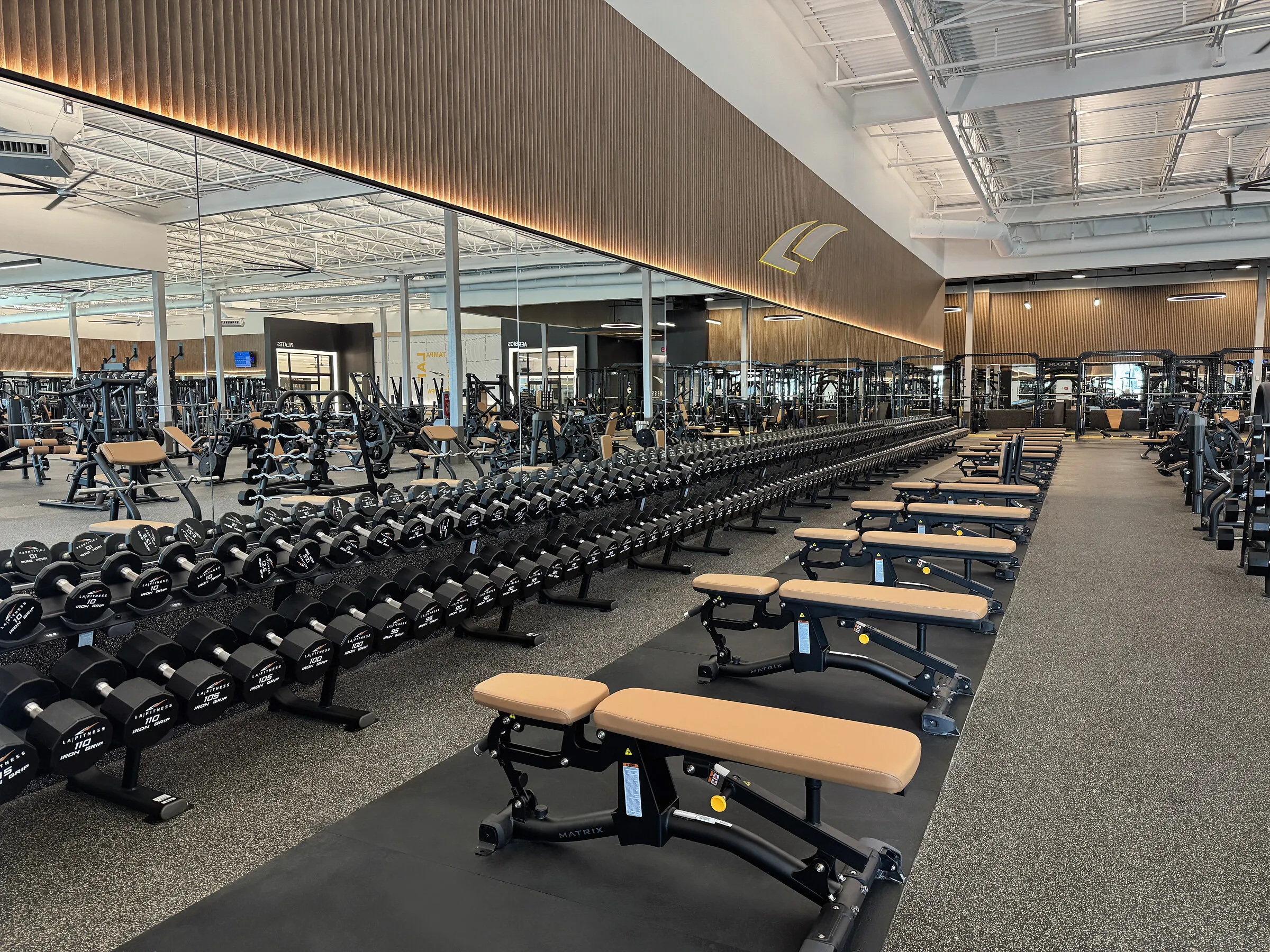 Rows of dumbbells, benches and strength-training equipment in a spacious gym.