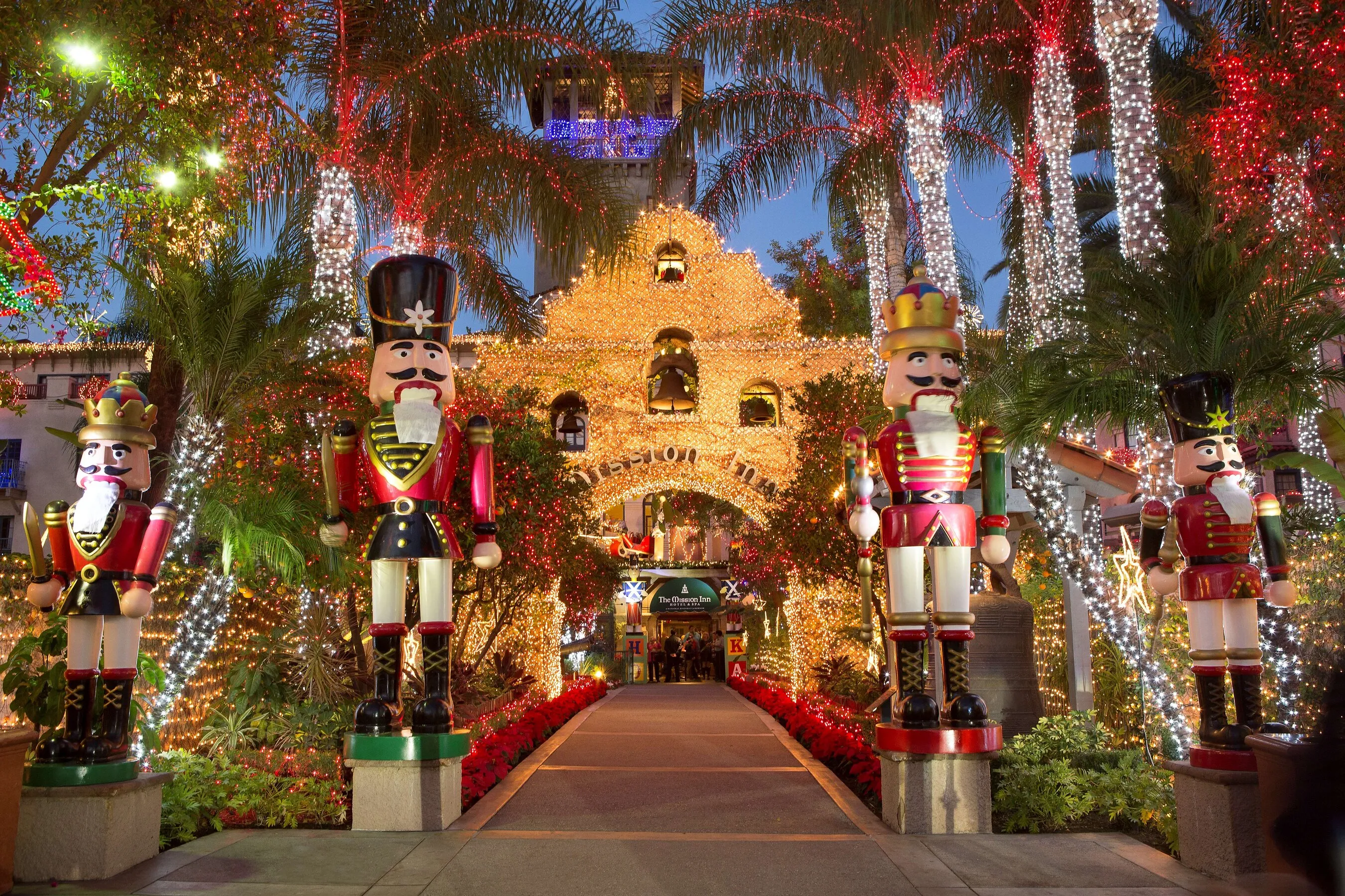 Nutcracker statues flank a brightly lit Christmas entrance lined with palm trees.