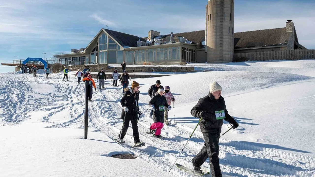 People snowshoeing through snow outside a resort during a winter race.