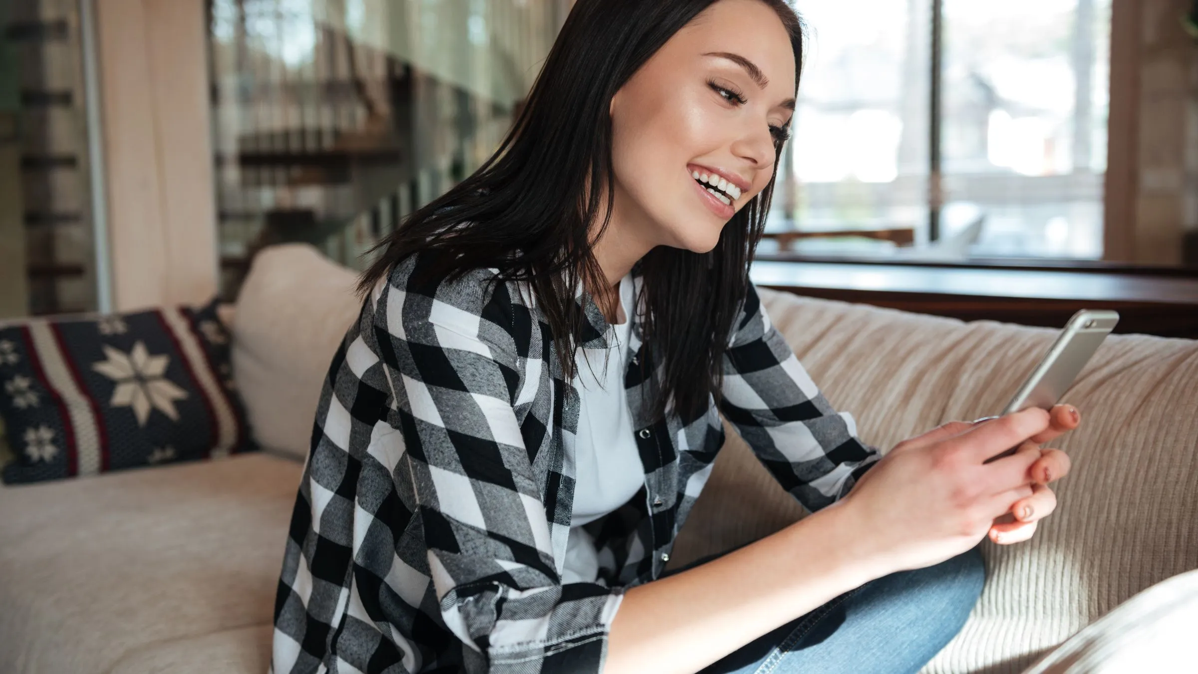 A woman on a sofa smiling at her phone.
