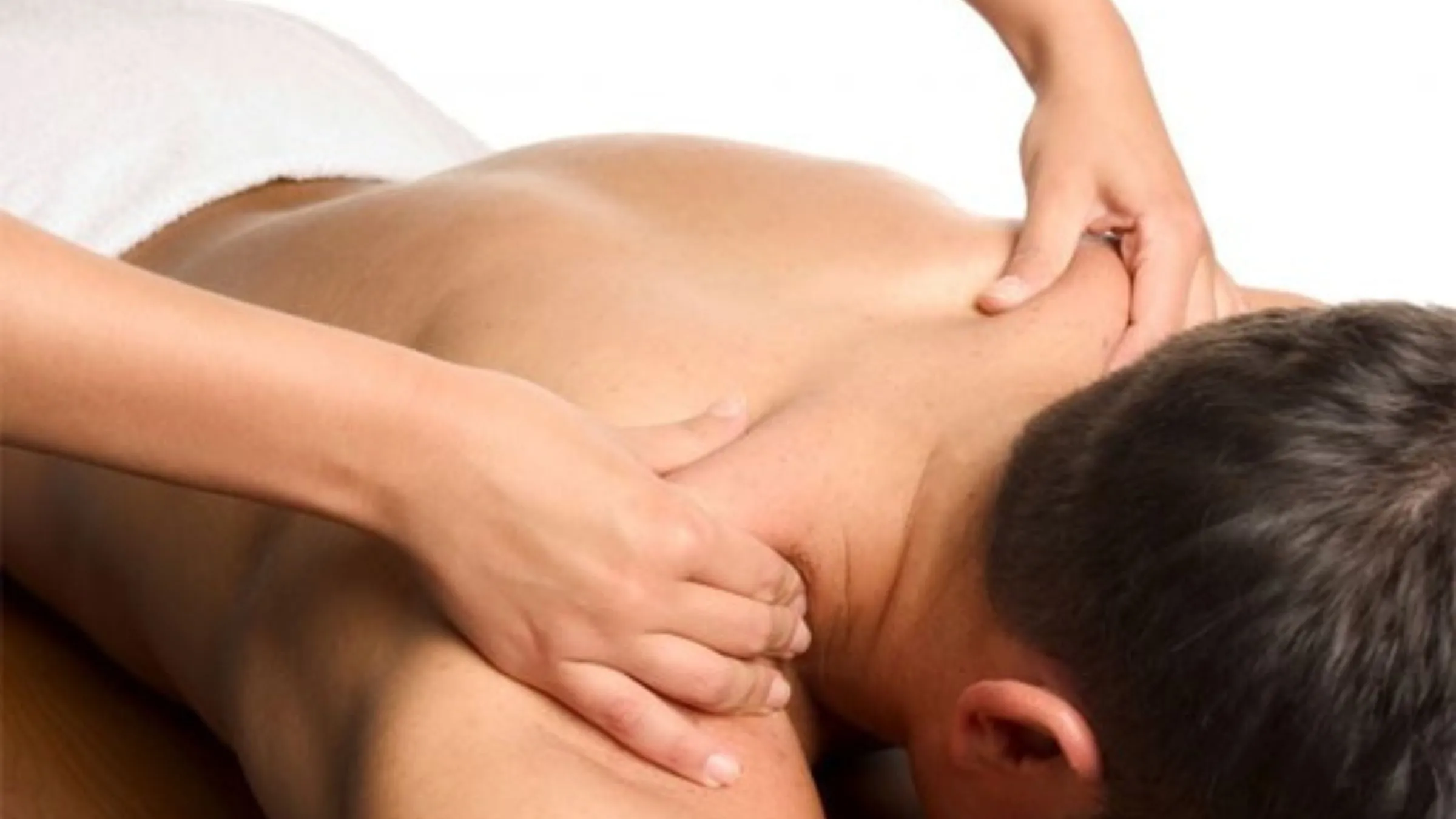 A massage therapist pressing on a man's shoulder during a back massage.