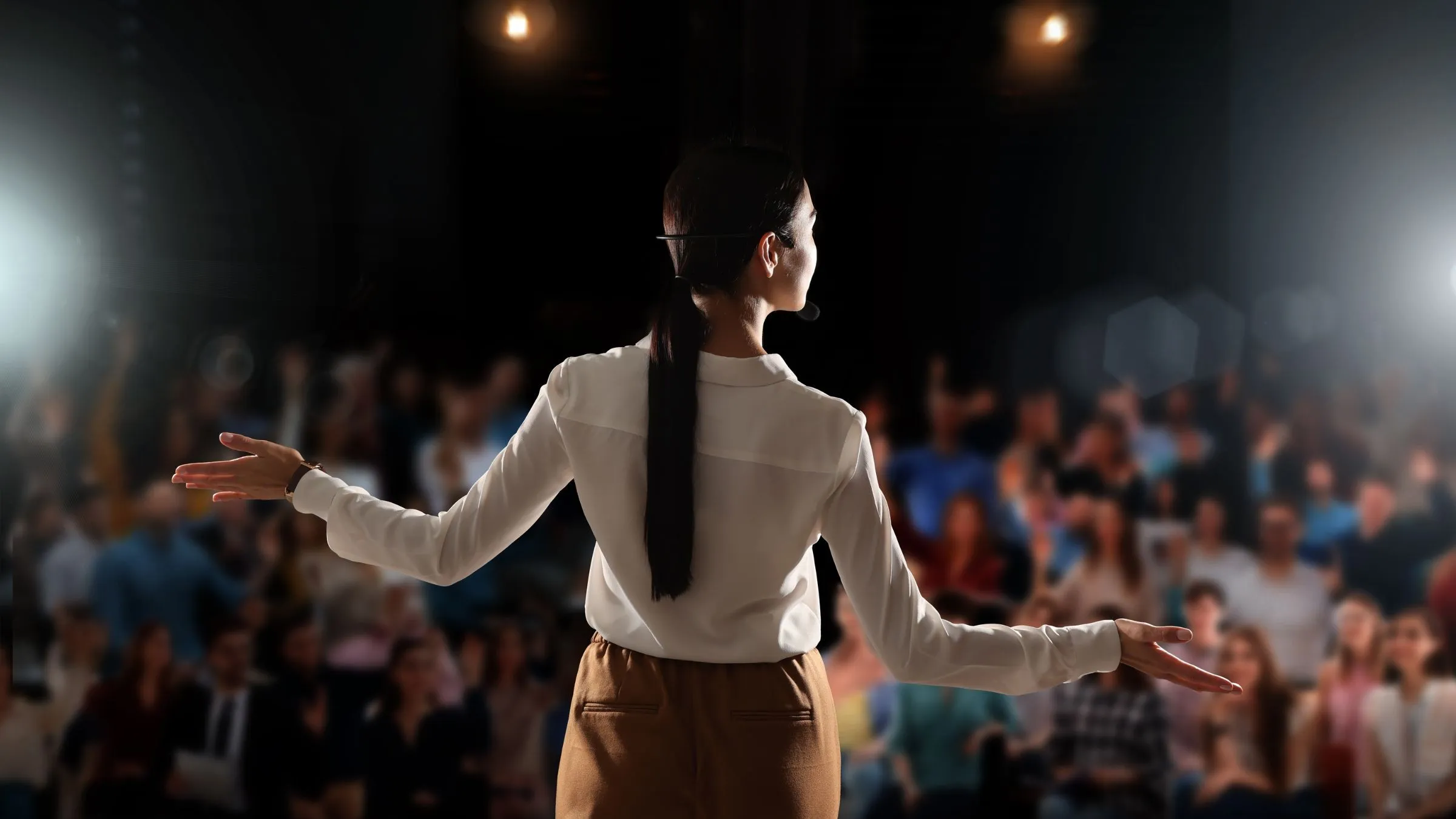 A speaker on a stage facing a large seated audience.