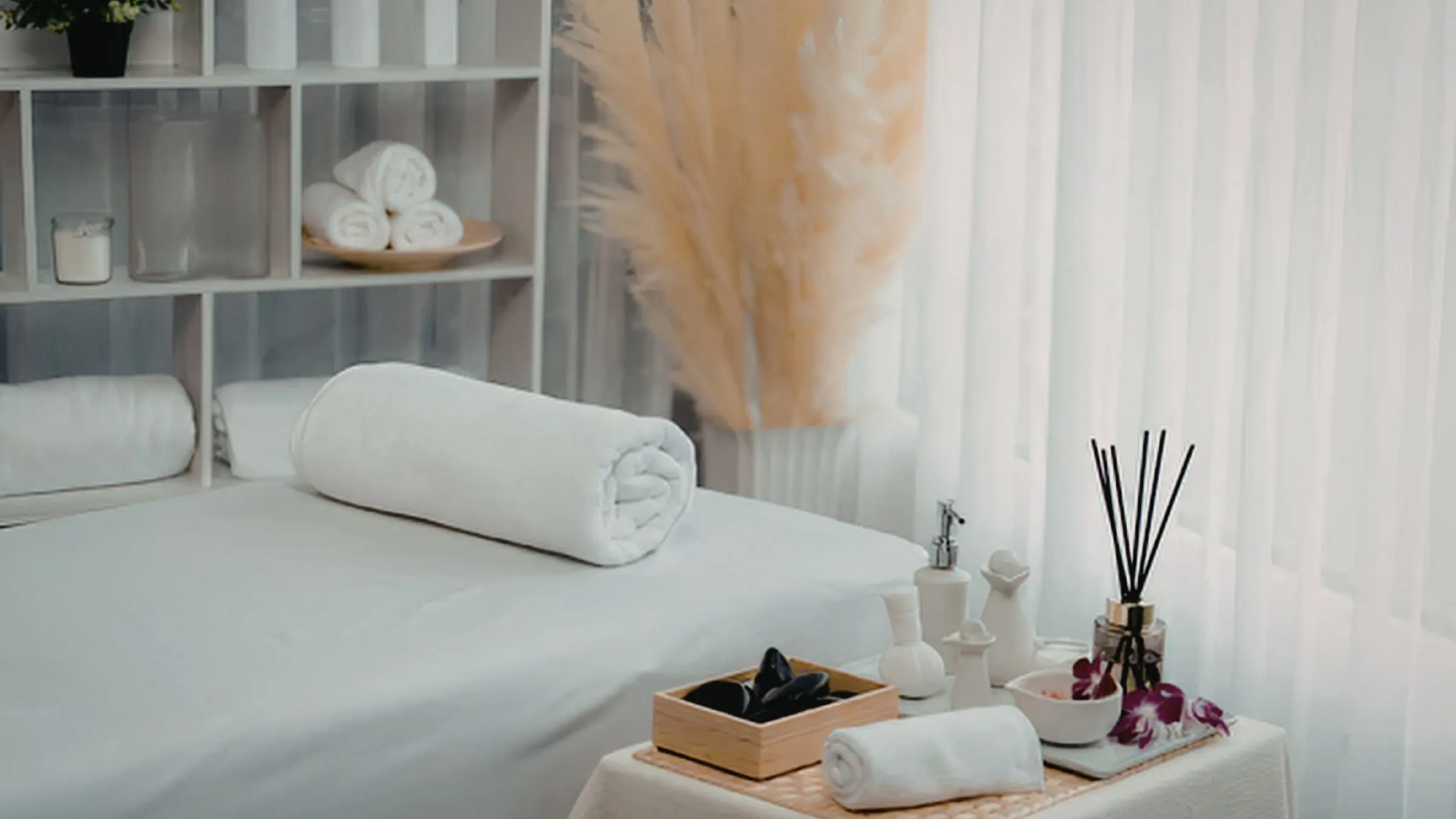 A white spa treatment table with rolled towels and a reed diffuser.