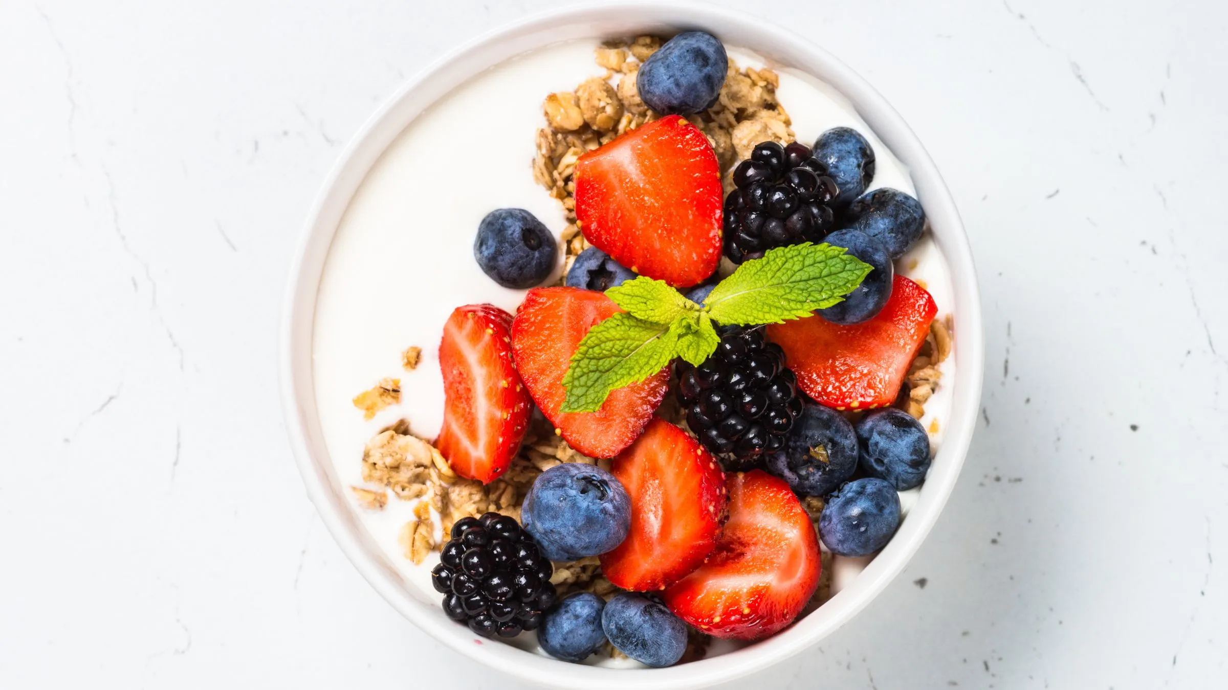 A bowl of yogurt and granola topped with strawberries, blueberries and mint.