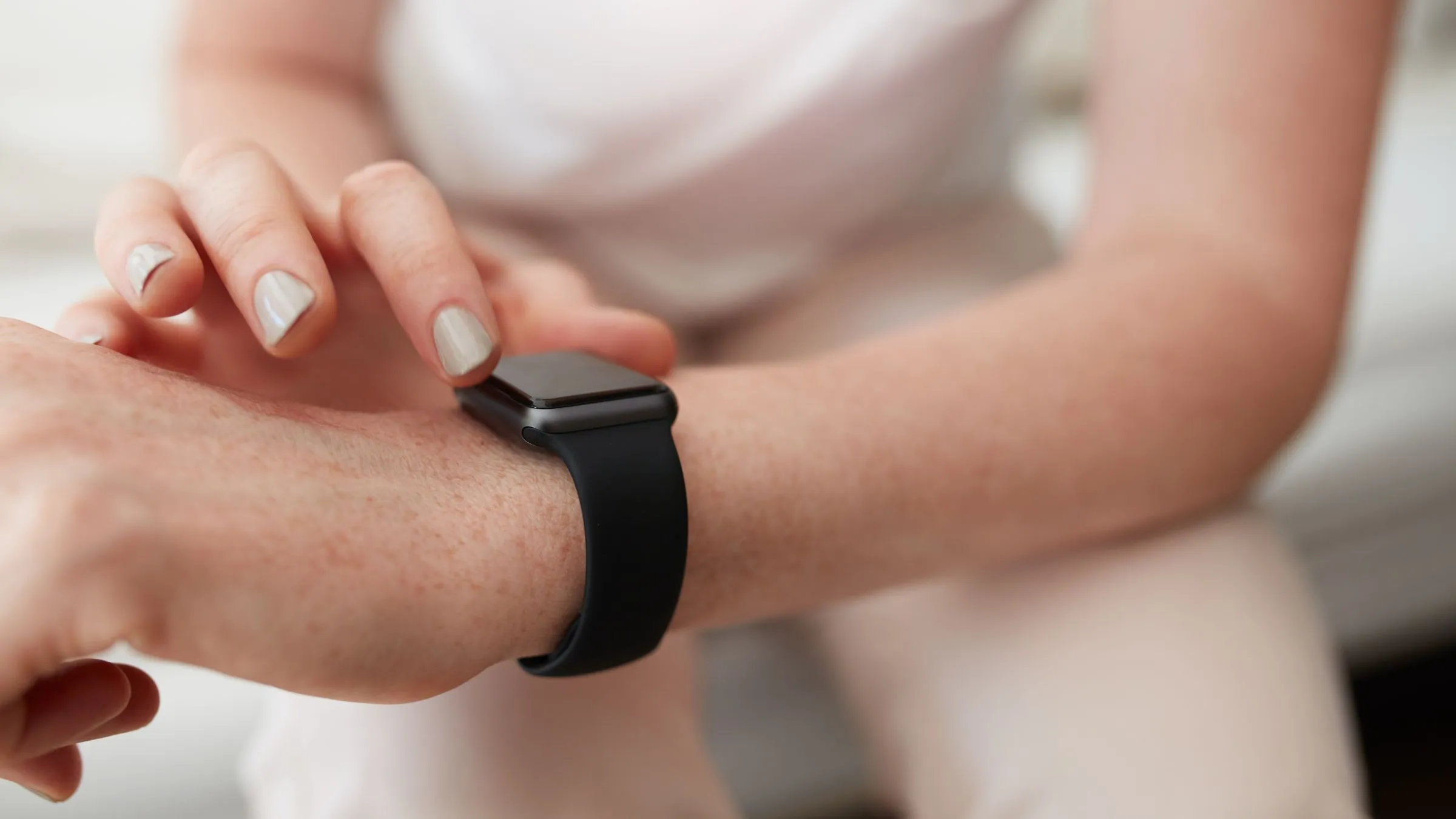 A woman touching the screen of a black smartwatch on her wrist.