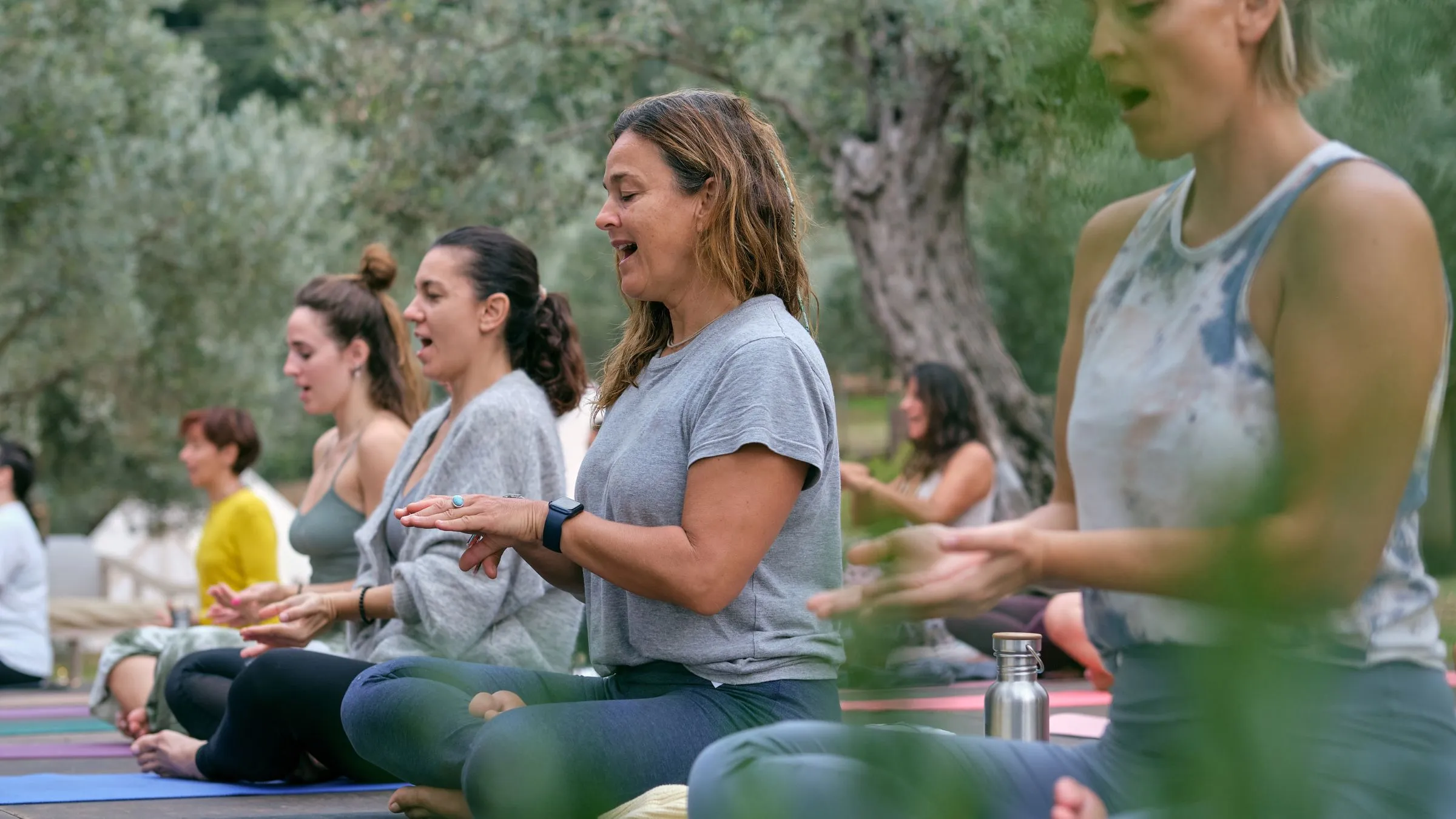 A group doing breathing exercises on yoga mats under olive trees.
