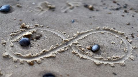 An infinity sign drawn in sand with small stones.