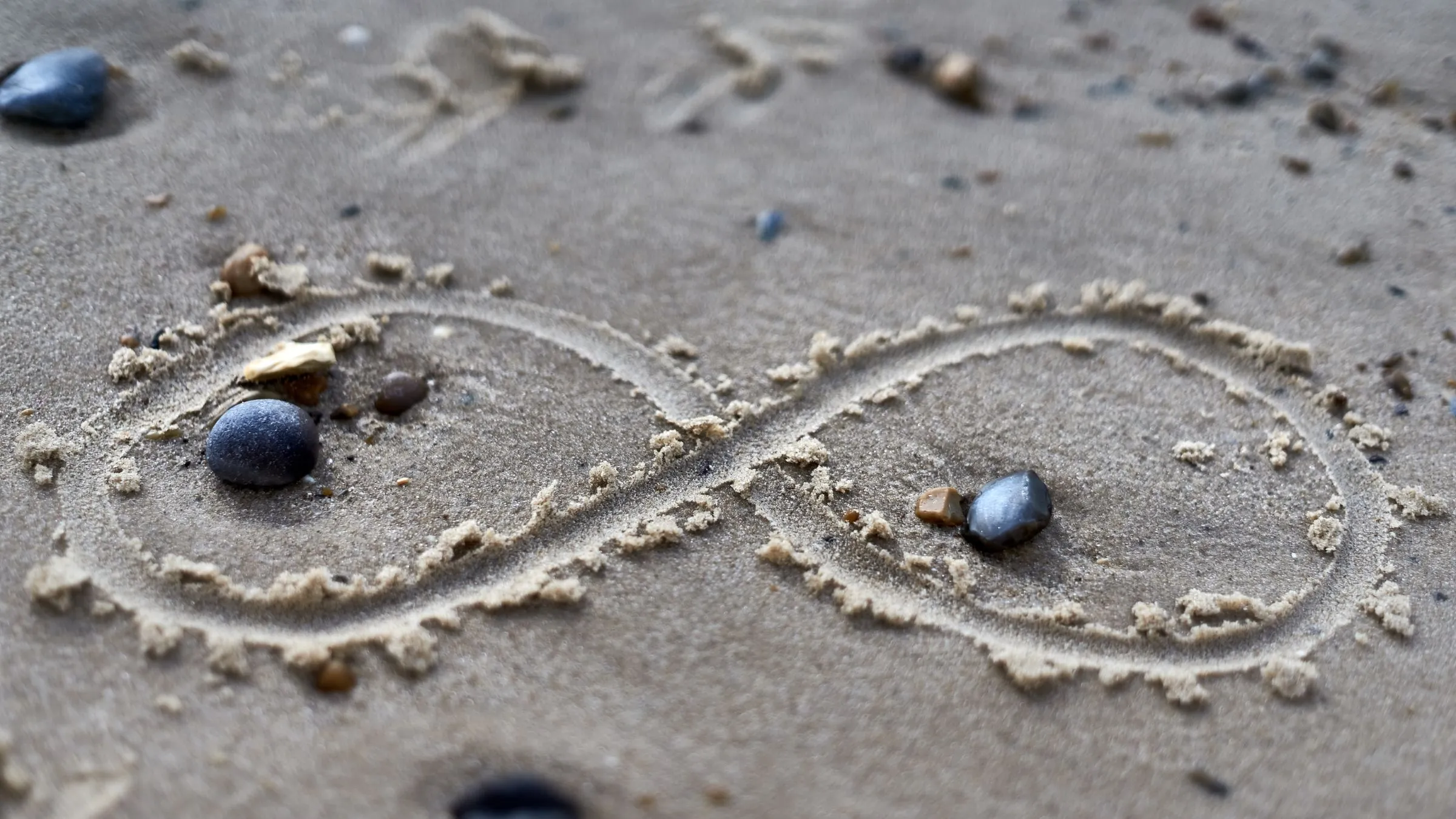 An infinity sign drawn in sand with small stones.