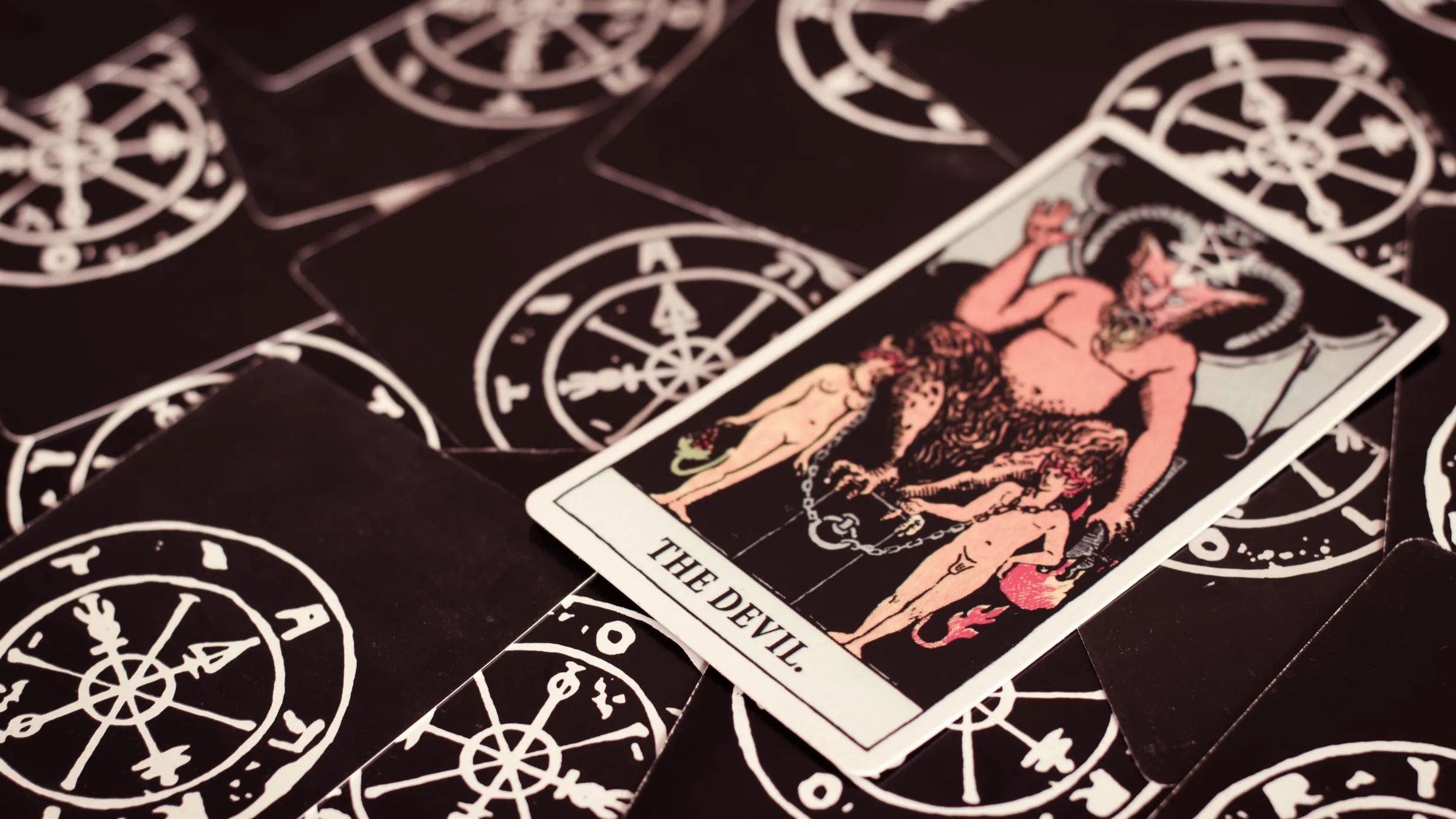 The Devil tarot card lying on black patterned card backs.