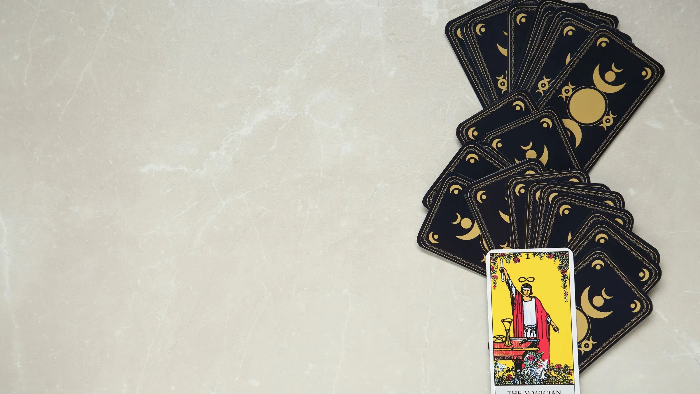 The Magician tarot card below a fan of dark card backs on pale marble.