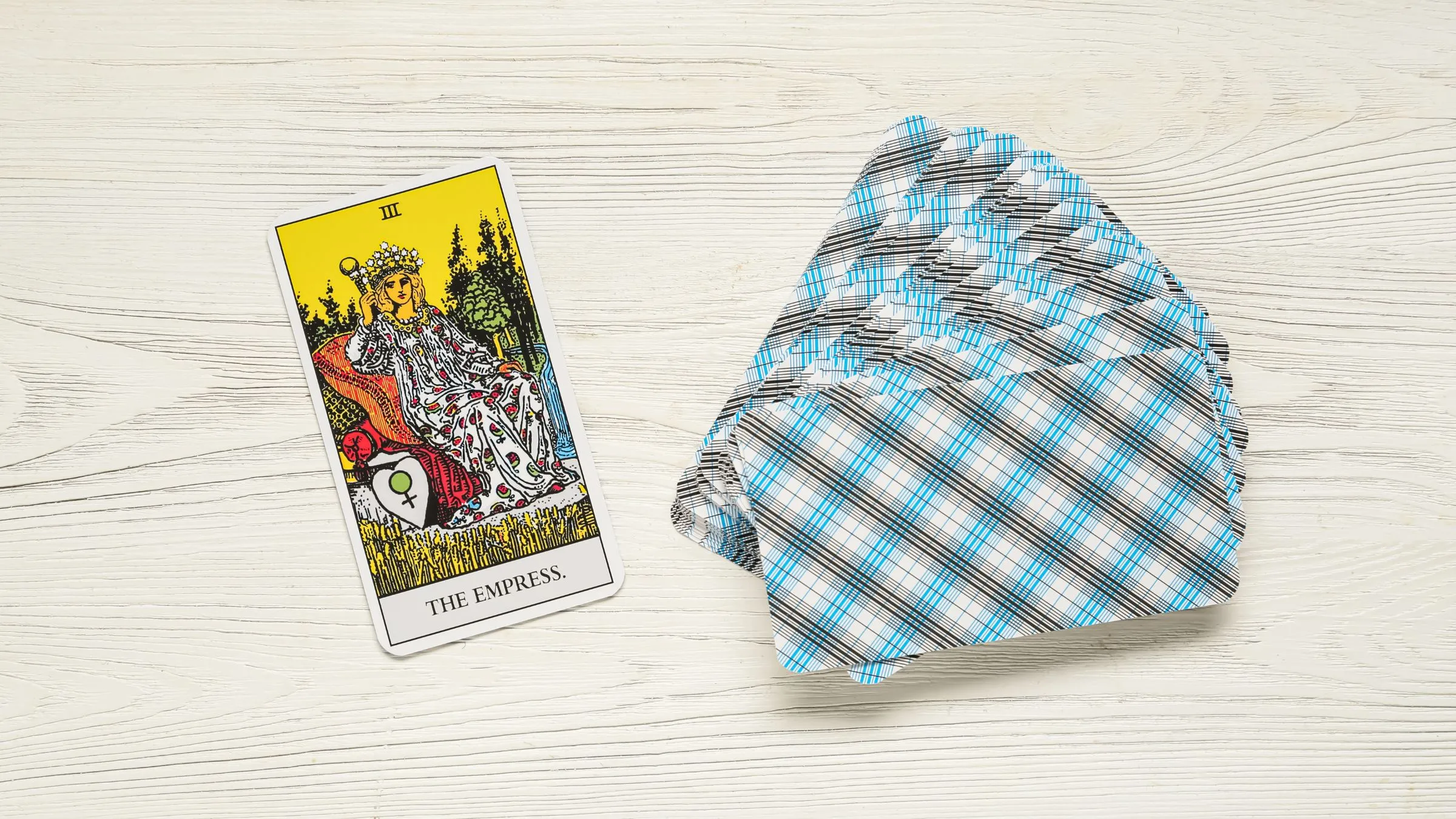 The Empress tarot card beside a fan of checked card backs on white wood.