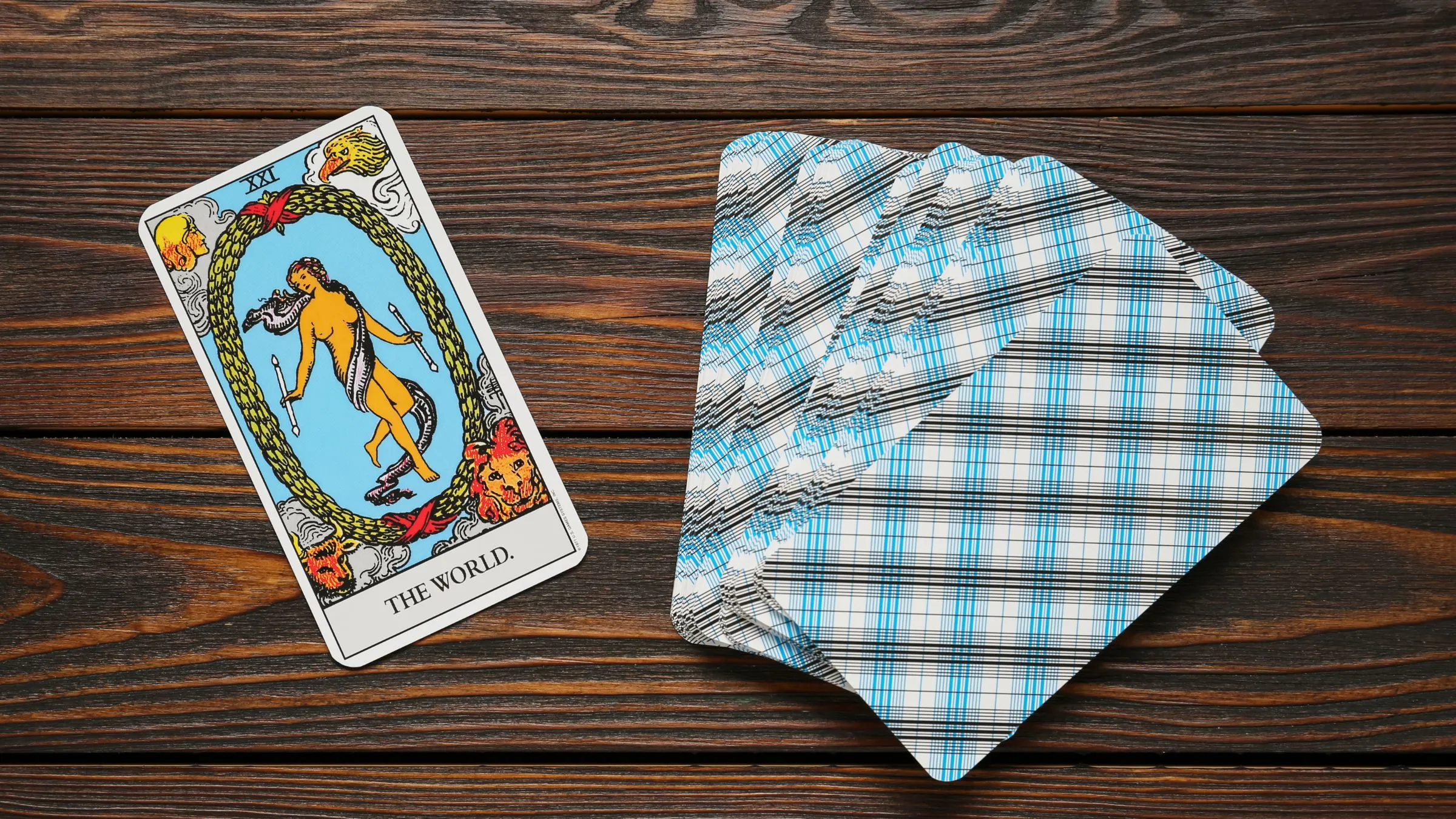 The World tarot card beside a fan of checked card backs on dark wood.