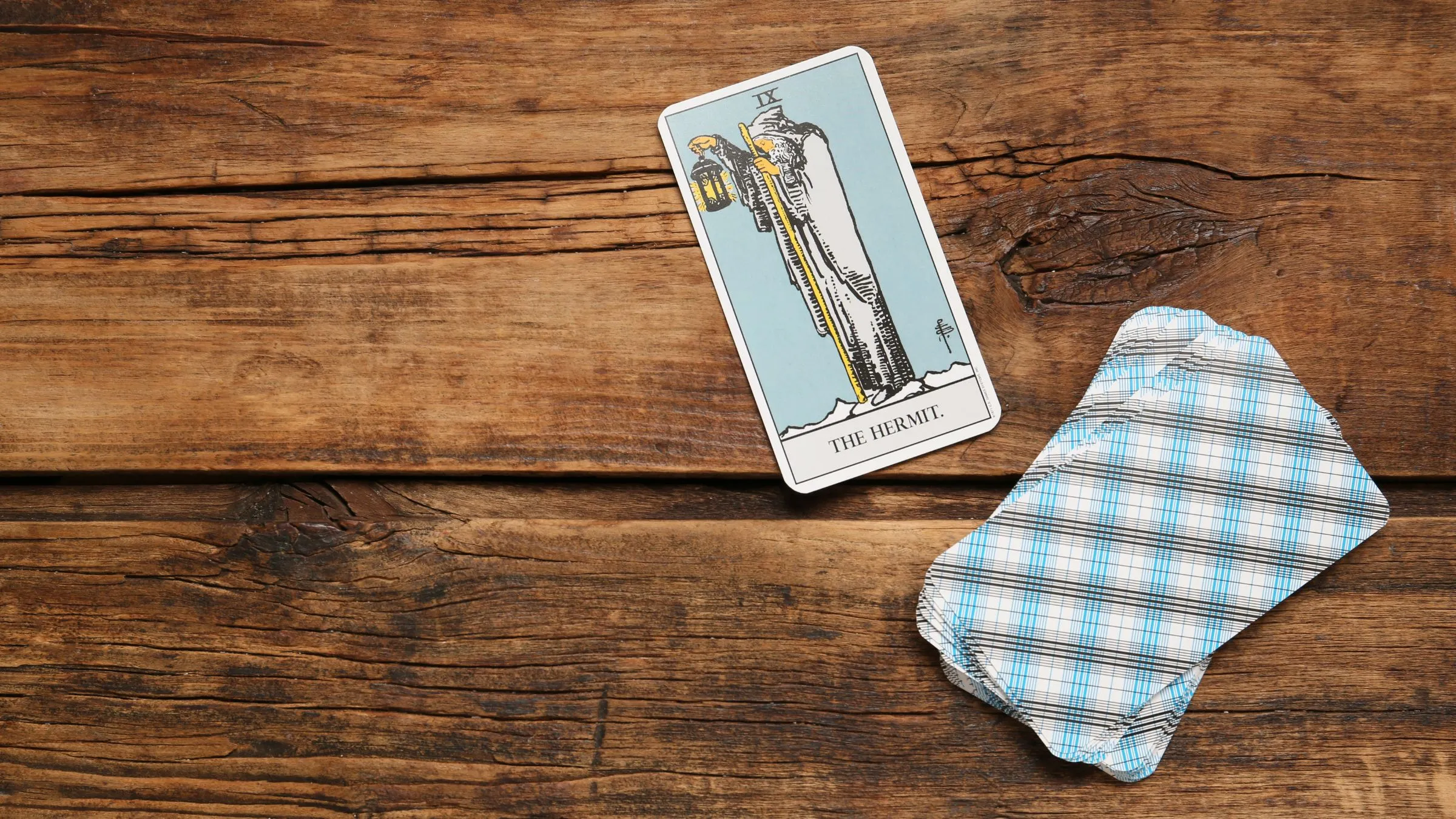 The Hermit tarot card beside a small deck on wooden boards.