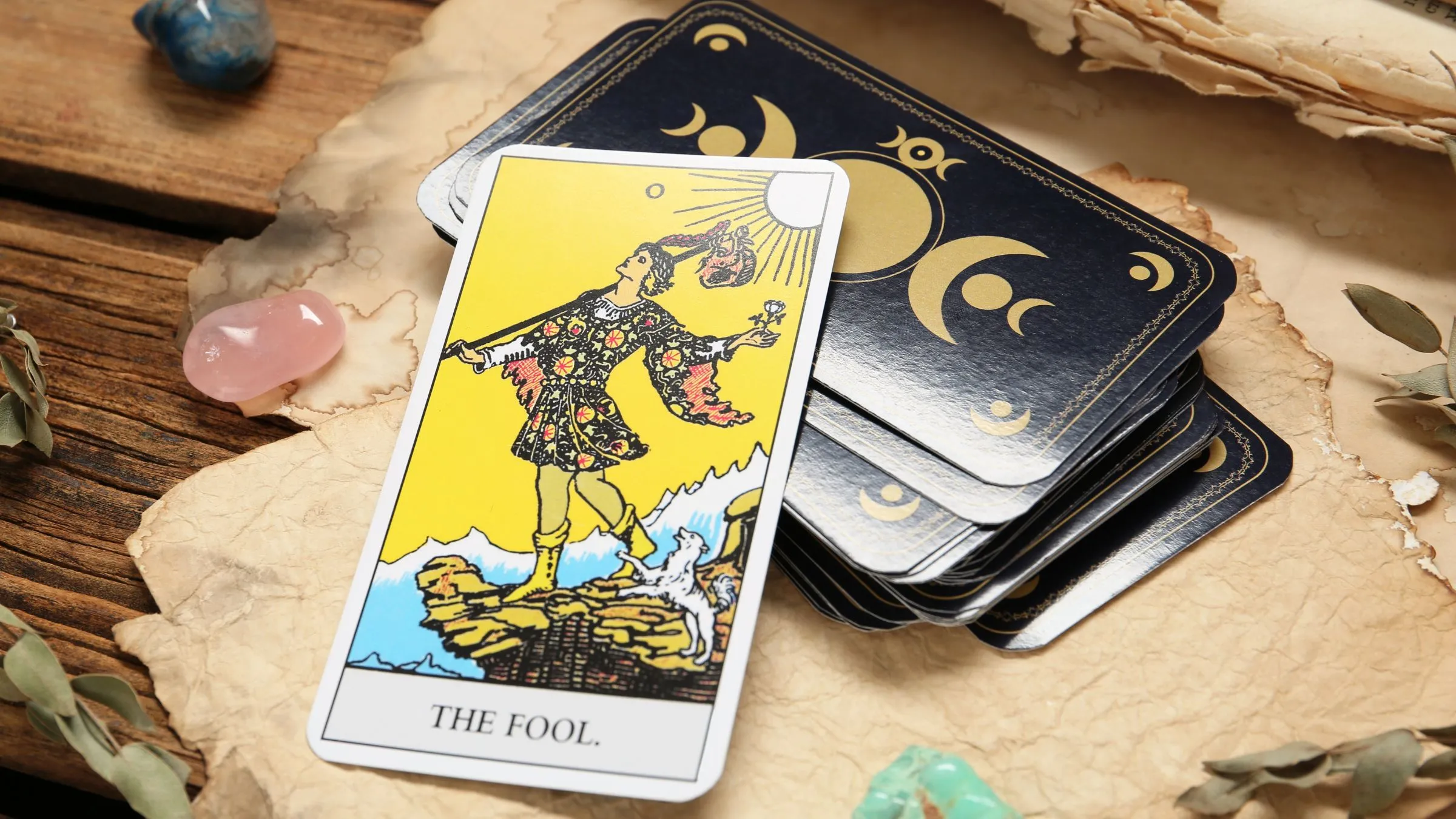 The Fool tarot card on a dark deck with crystals and old paper.