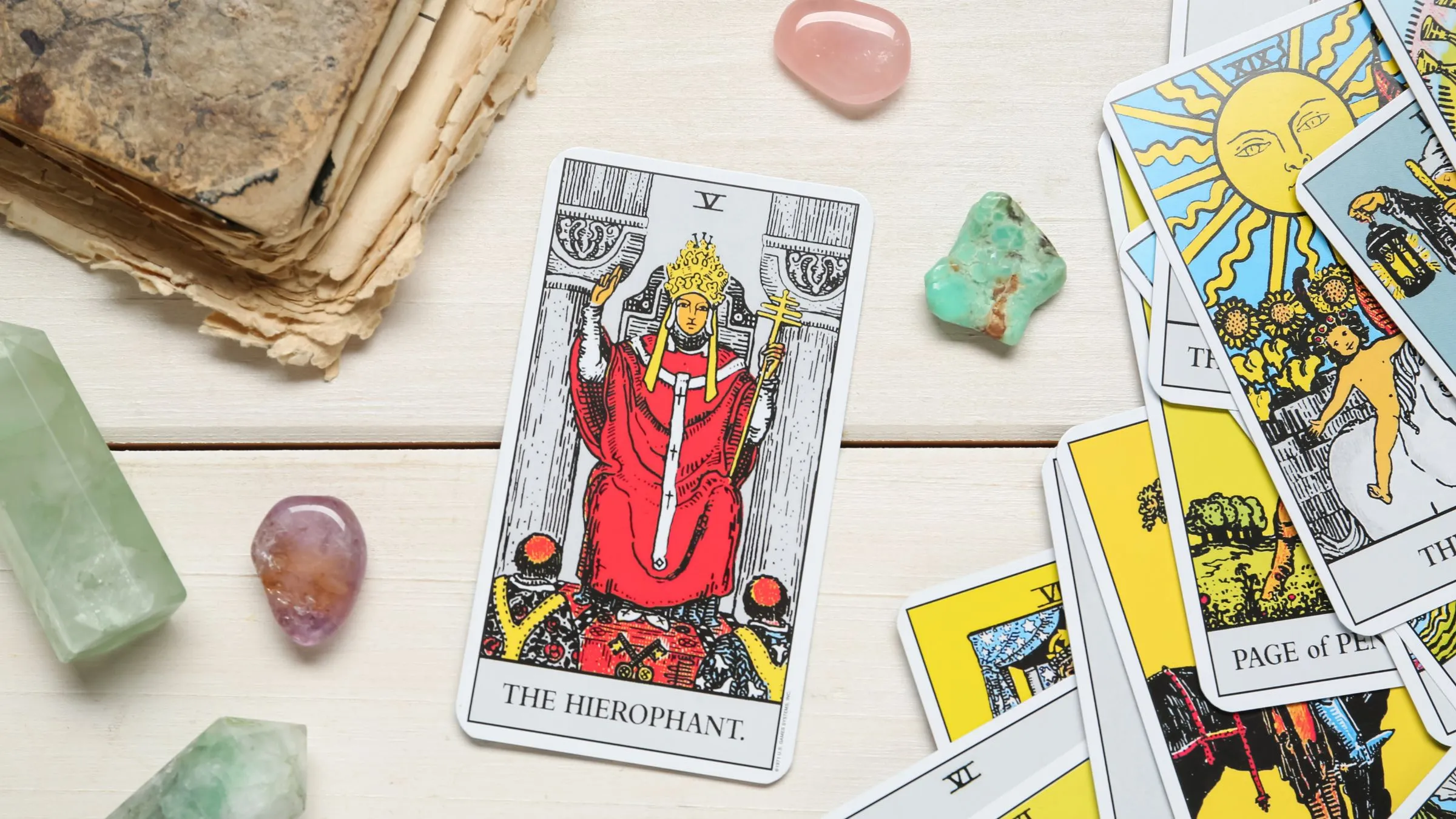 The Hierophant tarot card on white wood among crystals and other cards.