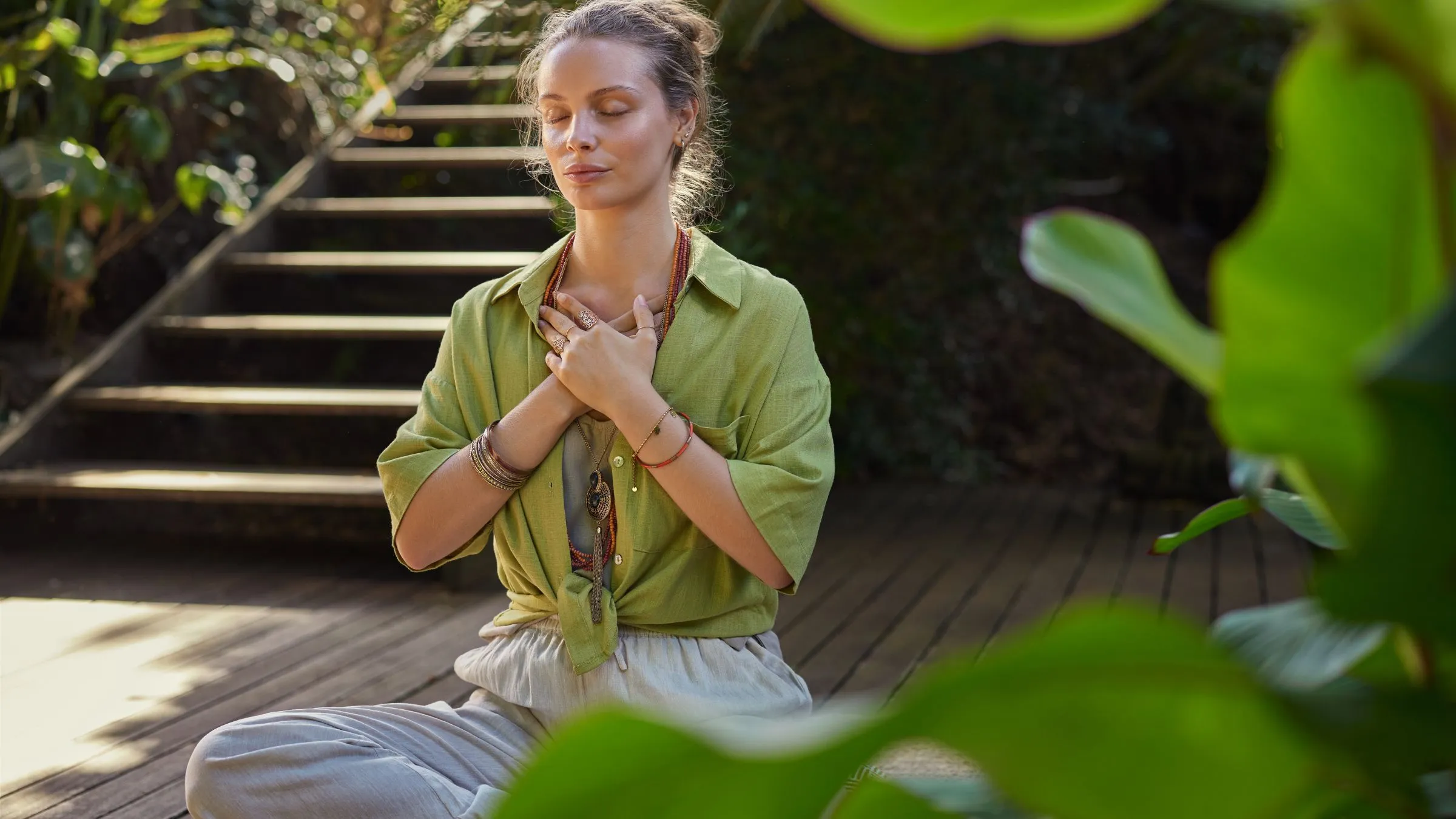 A woman meditating on a garden deck with her hands on her chest.