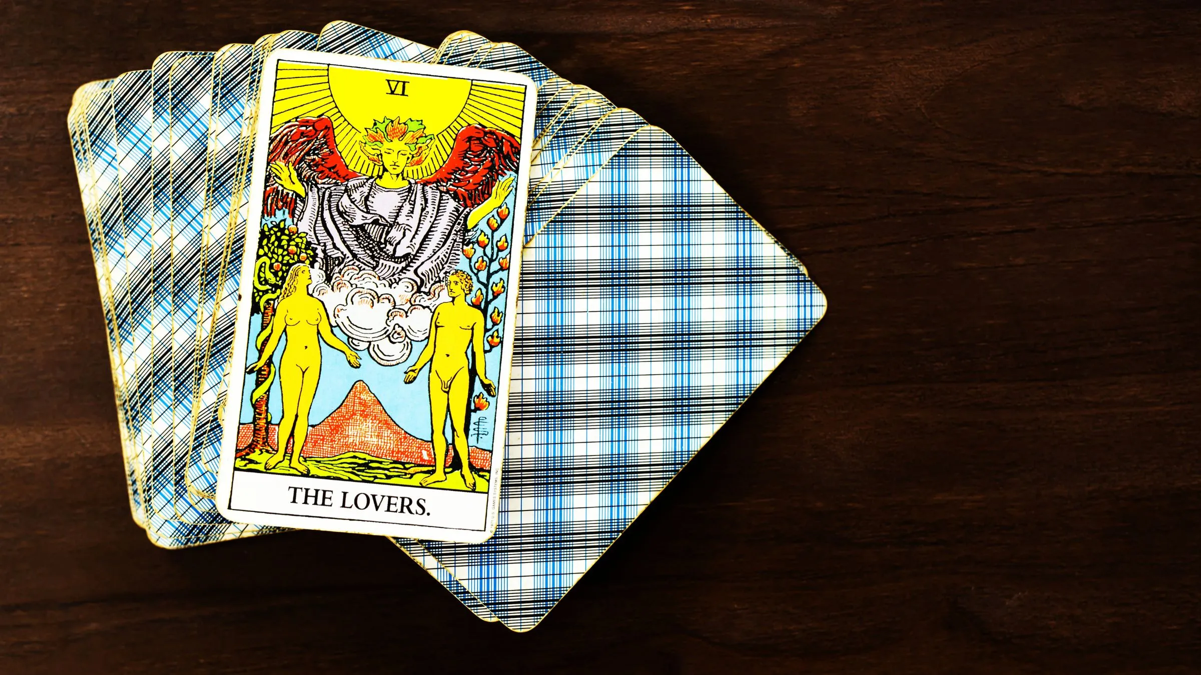 The Lovers tarot card on top of a fanned deck on dark wood.