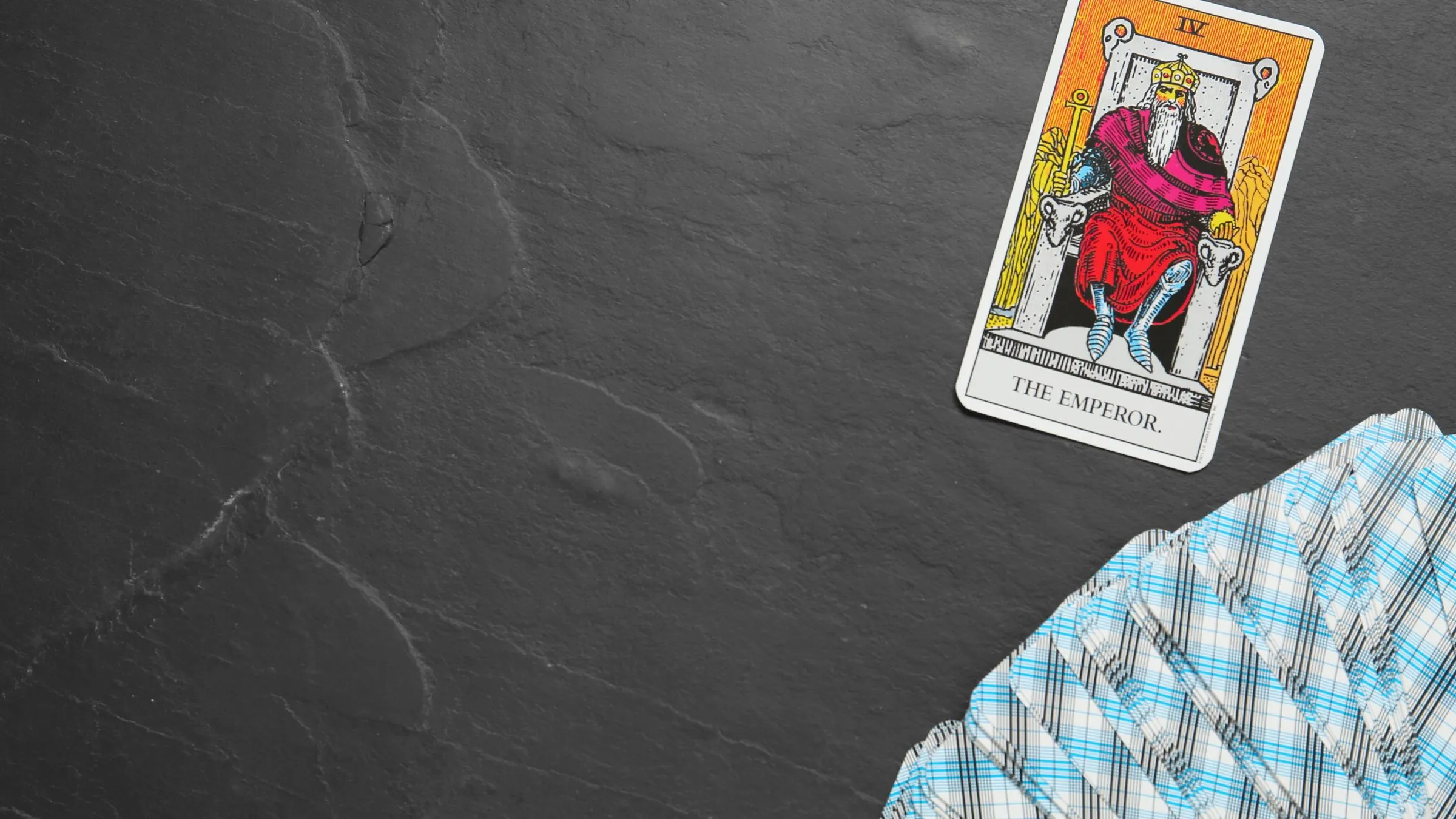 The Emperor tarot card on dark slate with a fan of card backs.