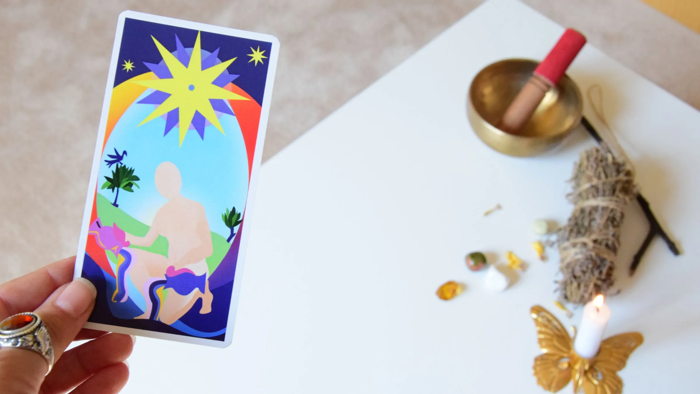 A hand holding a star tarot card above a table with a singing bowl and candle.