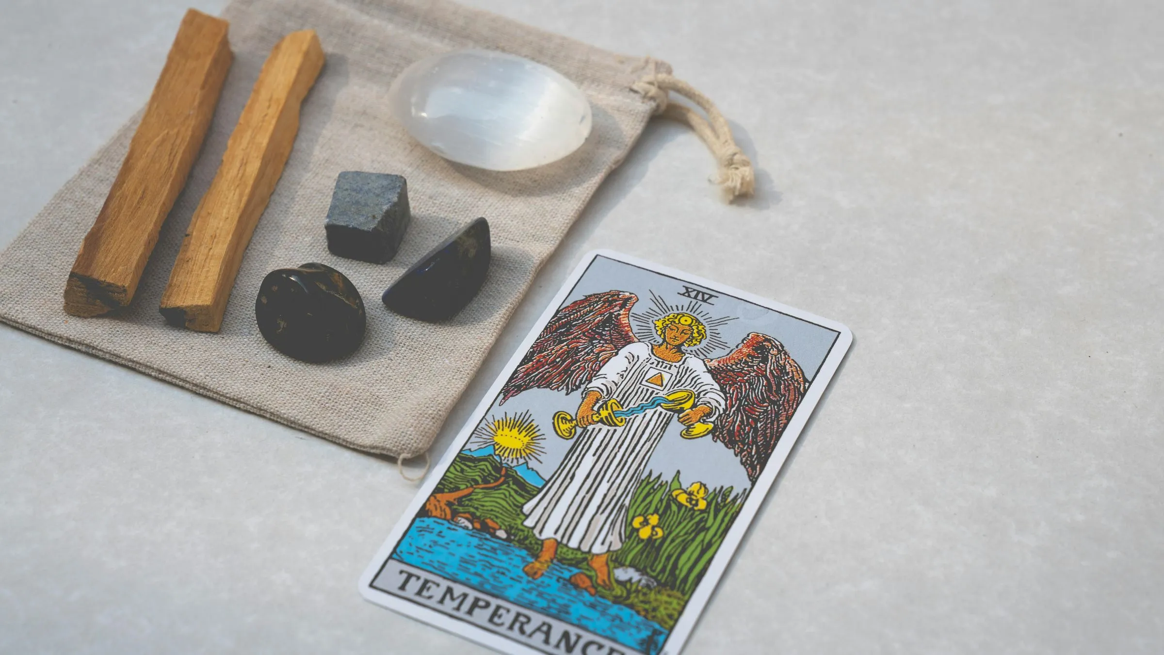 The Temperance tarot card beside crystals and palo santo sticks on a linen bag.