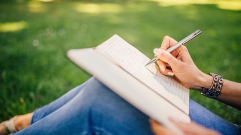 A person sitting on grass writing in a notebook.