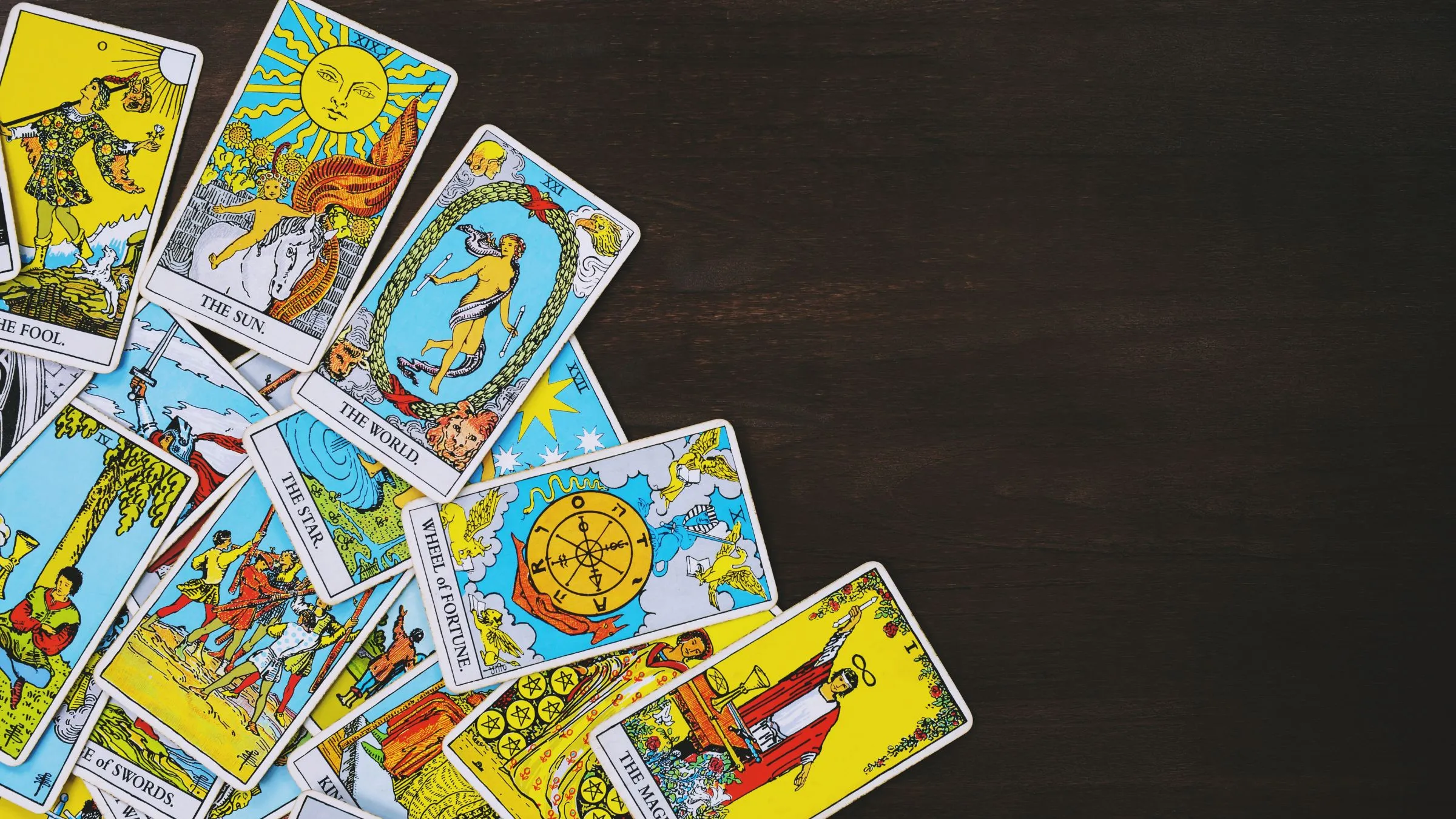 A scattered Rider-Waite tarot deck on dark wood.