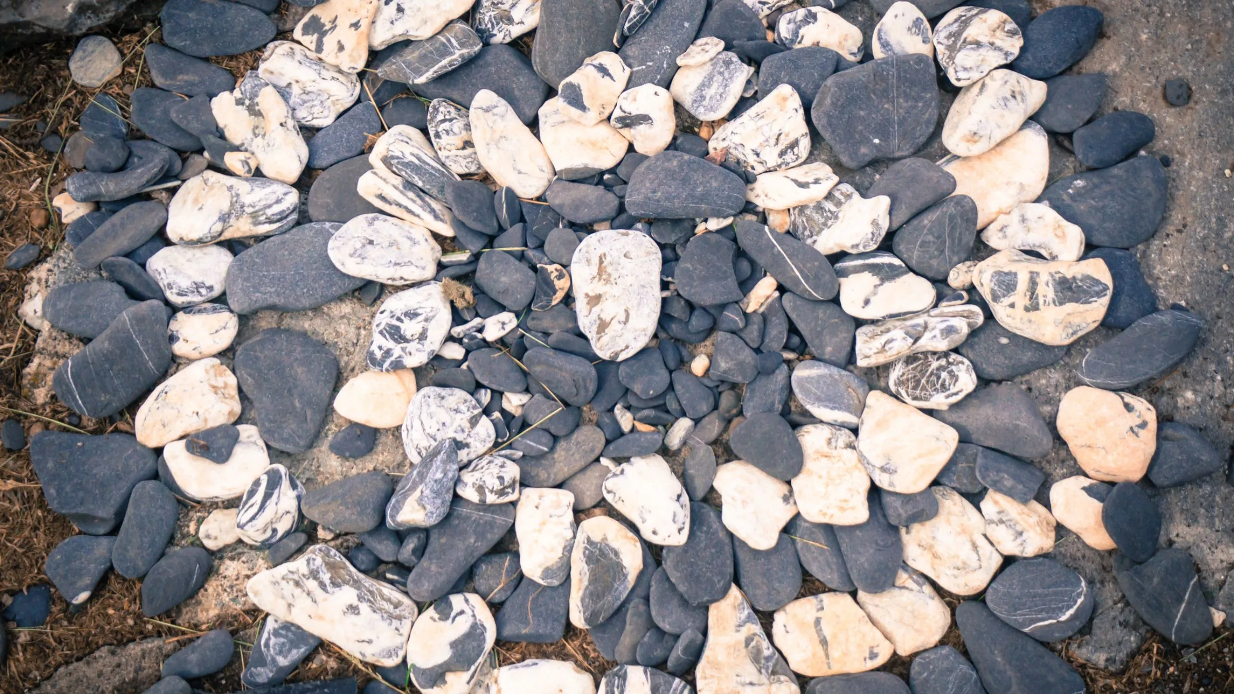 Pale and dark beach pebbles laid out in a spiral of circles.