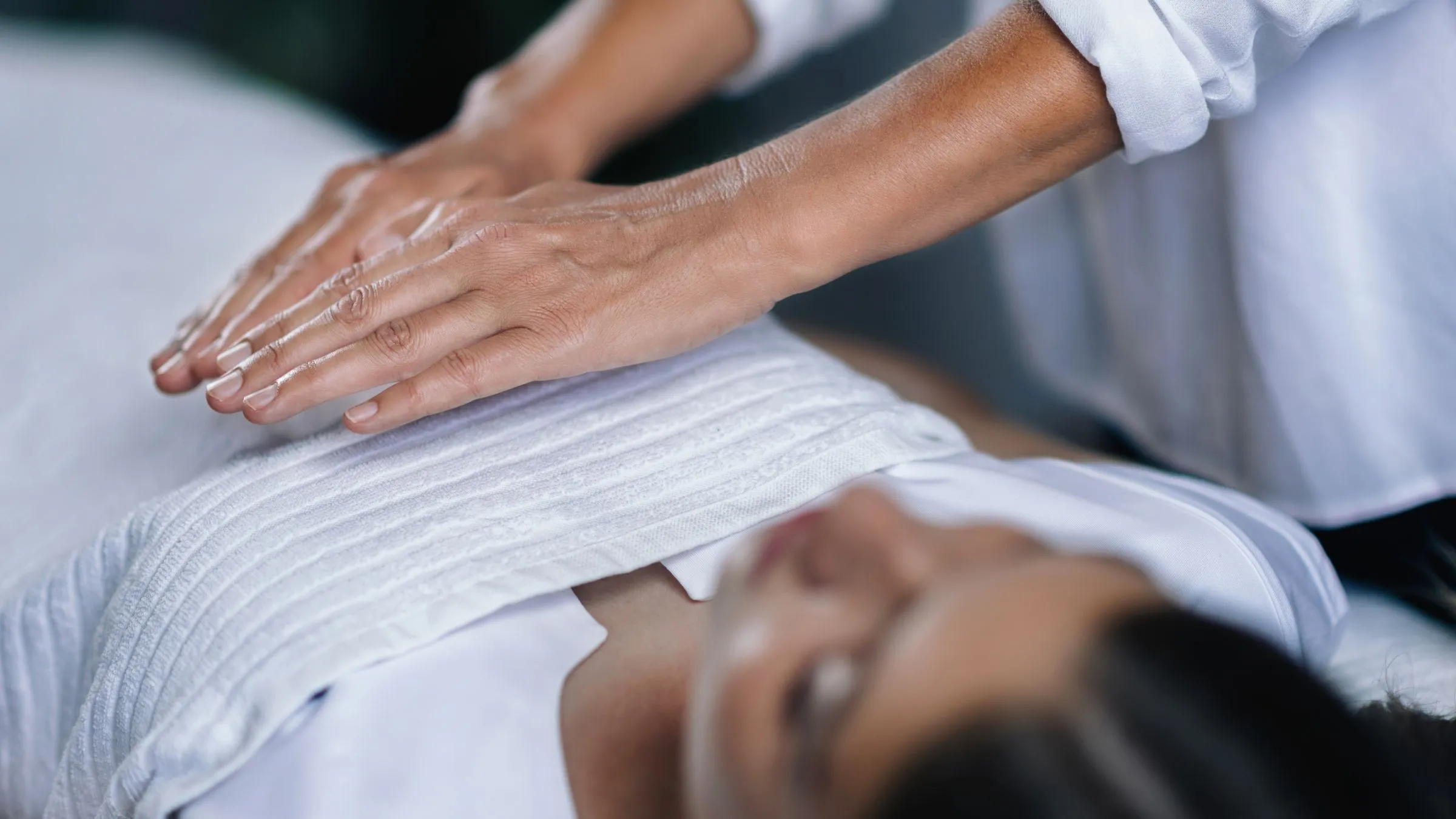 A practitioner holding her hands just above a woman lying on a treatment table.