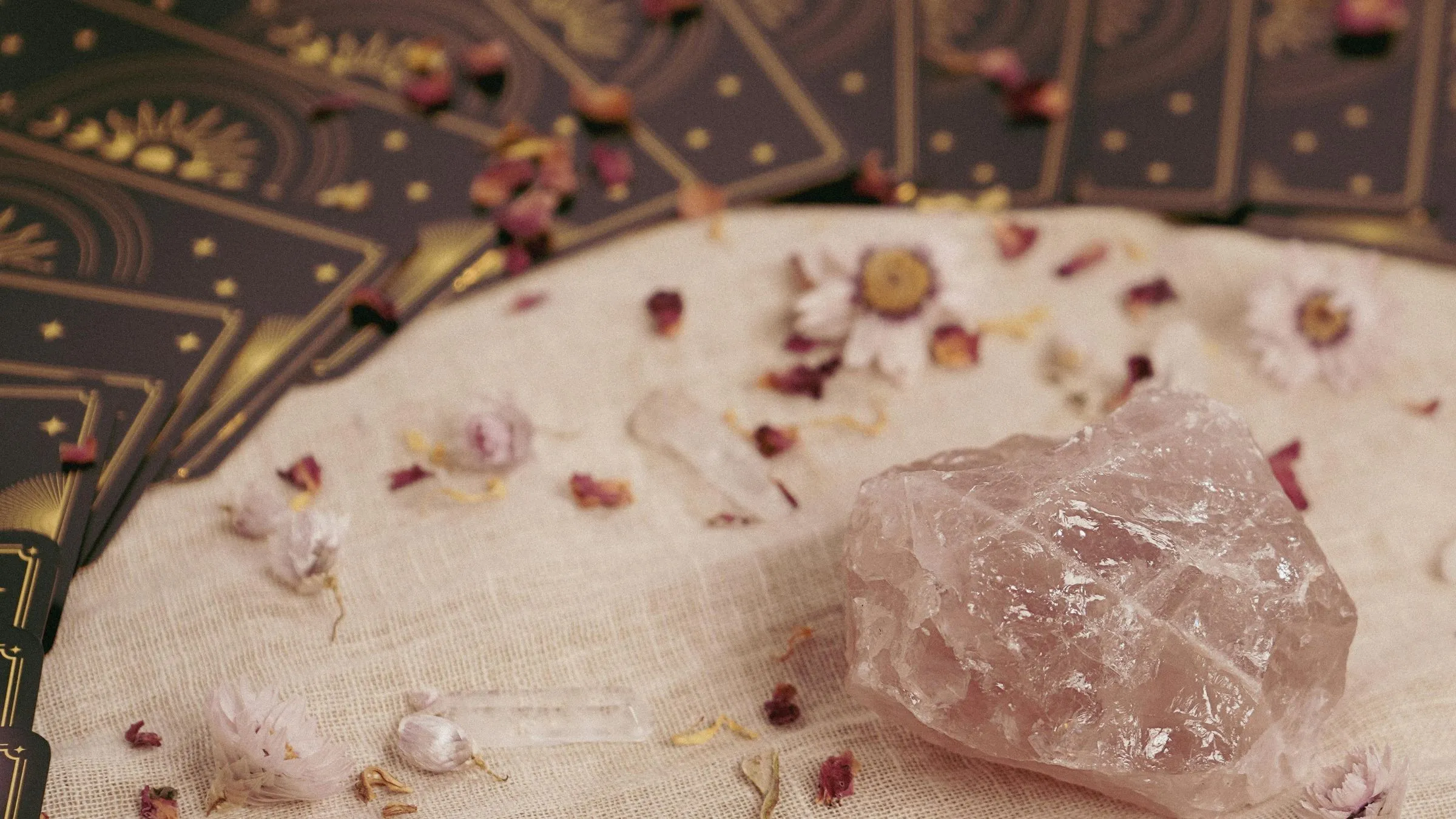 A rough rose quartz crystal on linen beside a spread of tarot card backs.