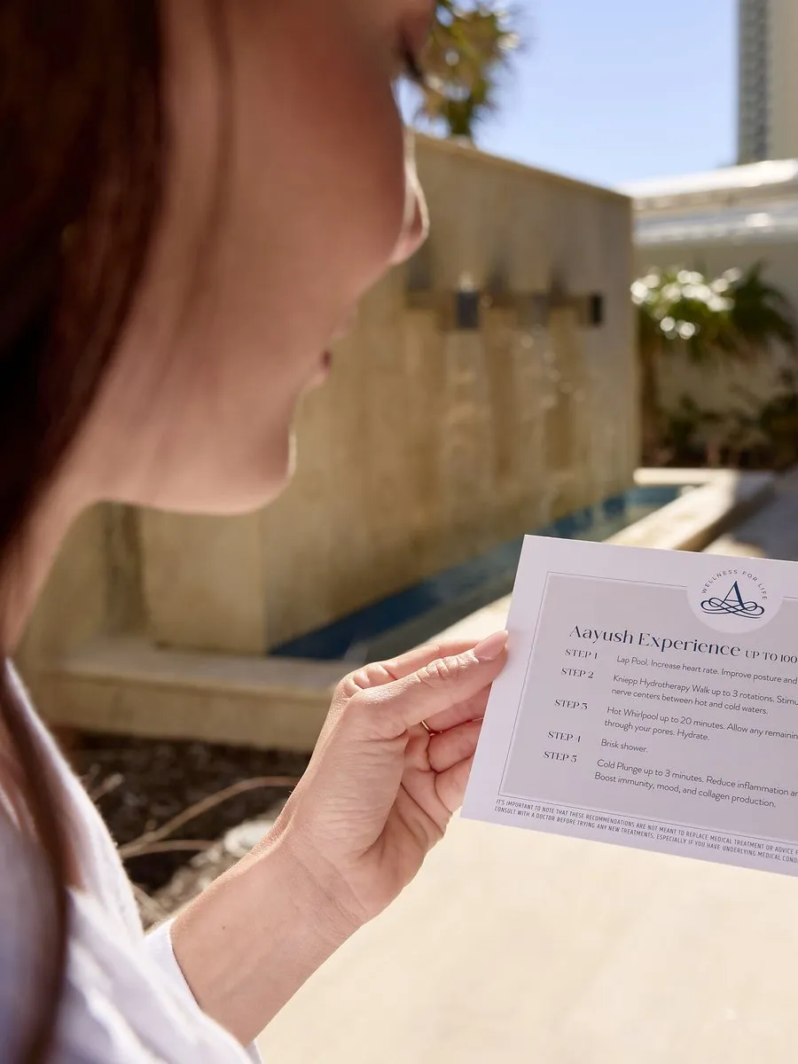 A person holds an Amrit Ocean Resort Spa treatment instruction card by a pool.
