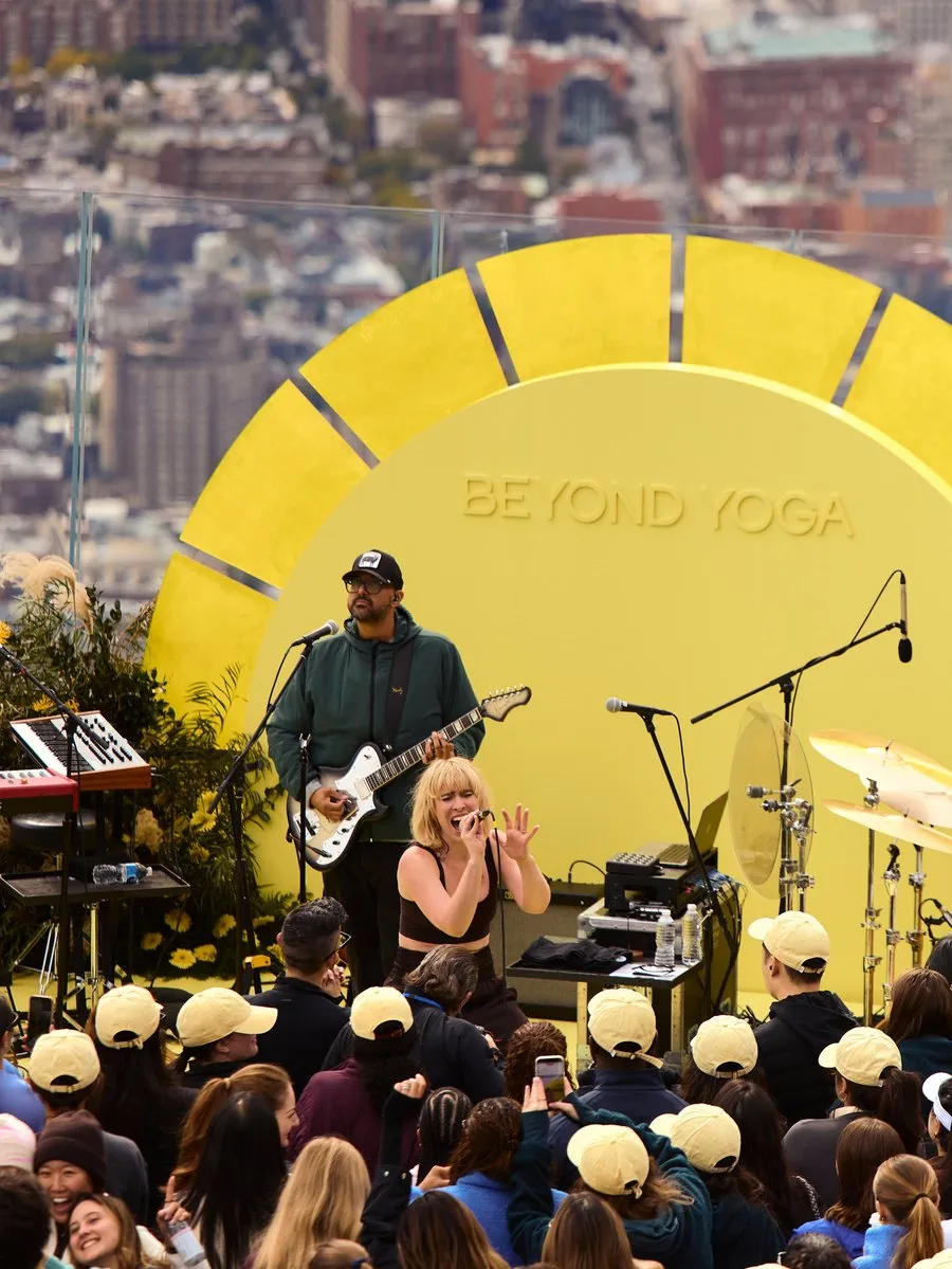 A singer and guitarist perform before a crowd at a yellow Beyond Yoga stage.