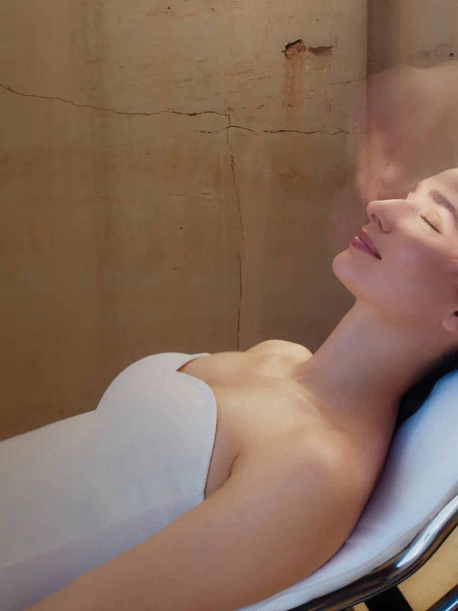 A person relaxes on a spa treatment bed while hands massage her temples.